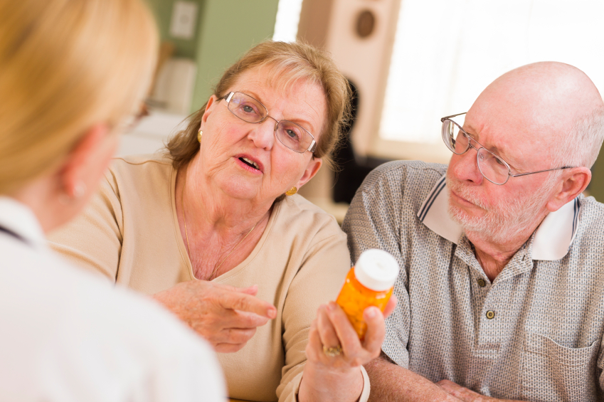 Doctor or Nurse Explaining Prescription Medicine to Attentive Senior Couple.