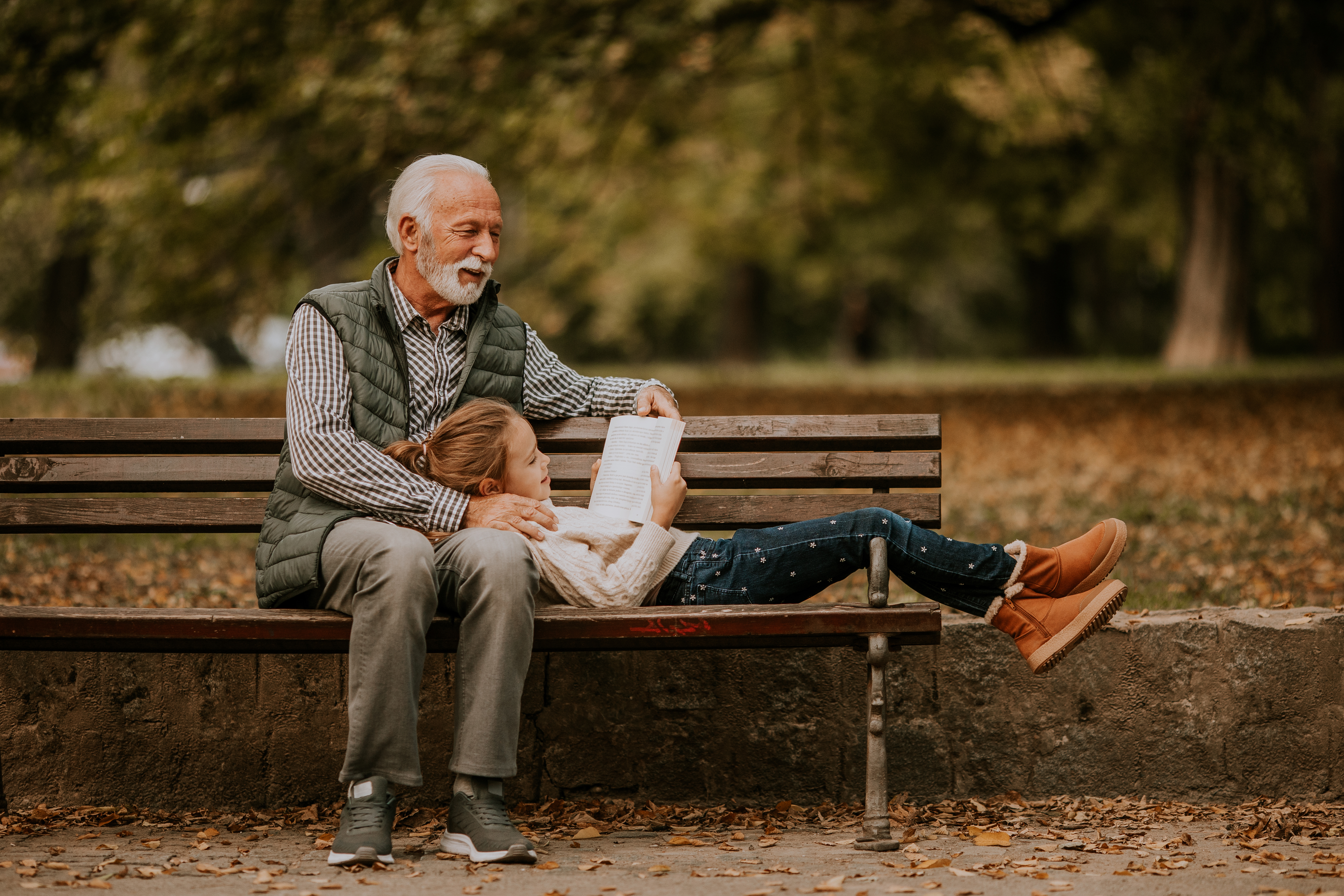 Grandfather spending time with his granddaughter on bench in park on autumn day