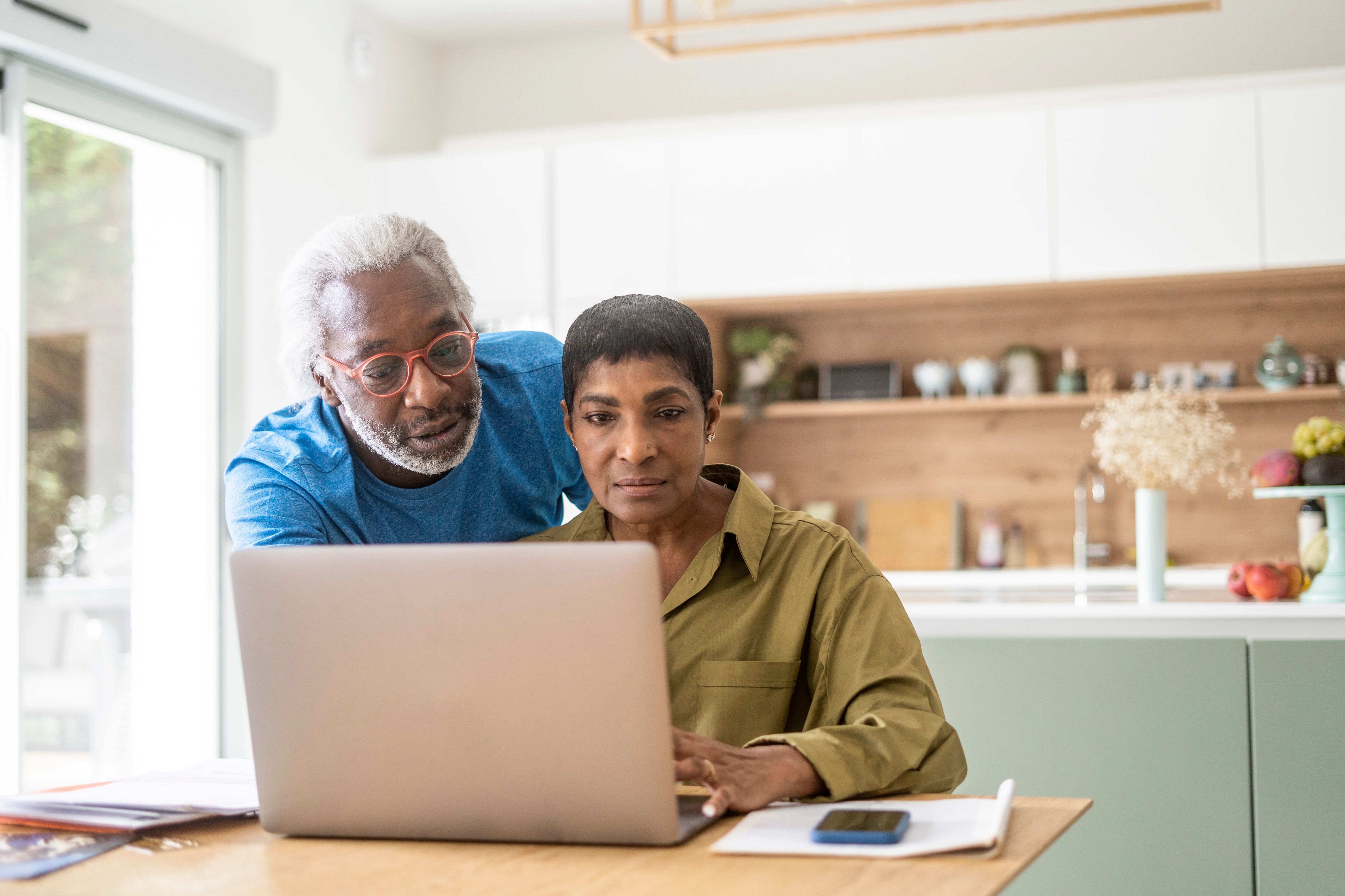 A Black couple at their kitchen table looking at laptop computer.