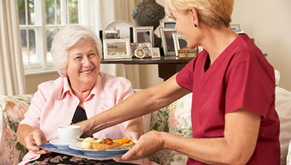 Helper Serving Senior Woman With Meal In Care Home