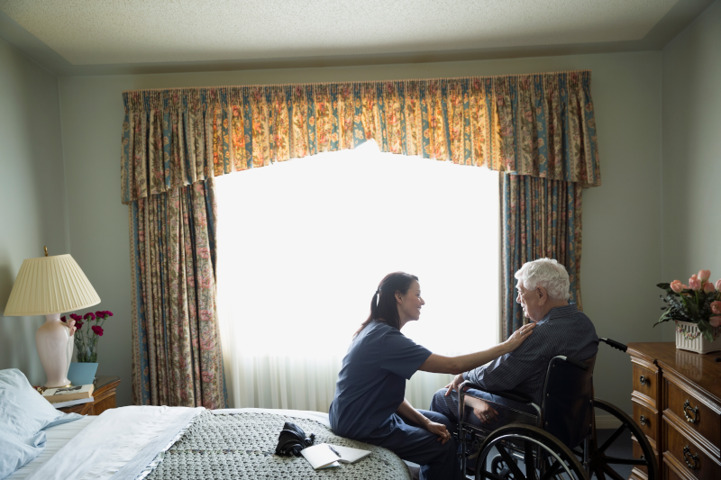 Healthcare professional comforts elderly woman in wheelchair. GettyImages-645424553 (1).png