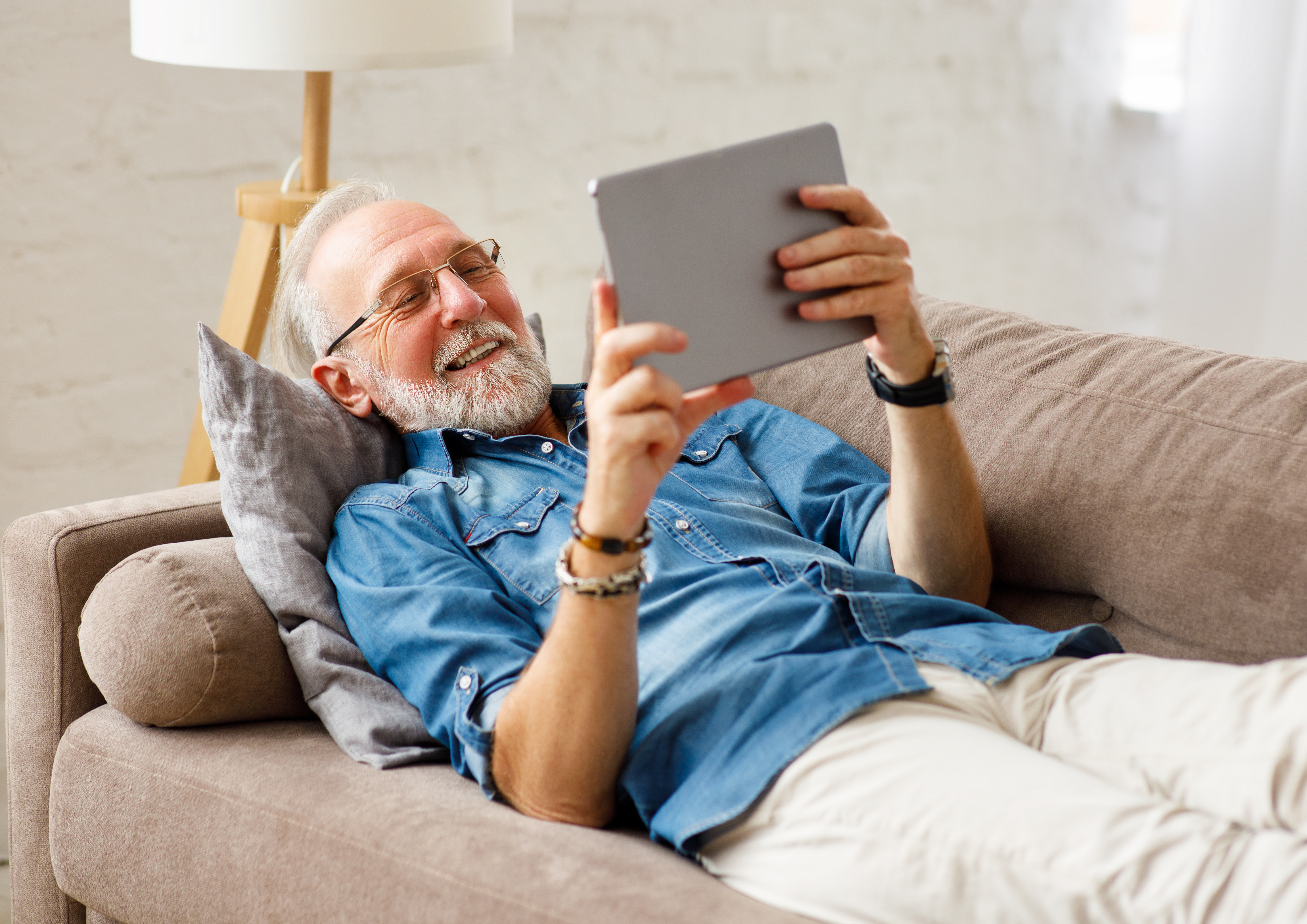 Cheerful aged man using tablet on couch