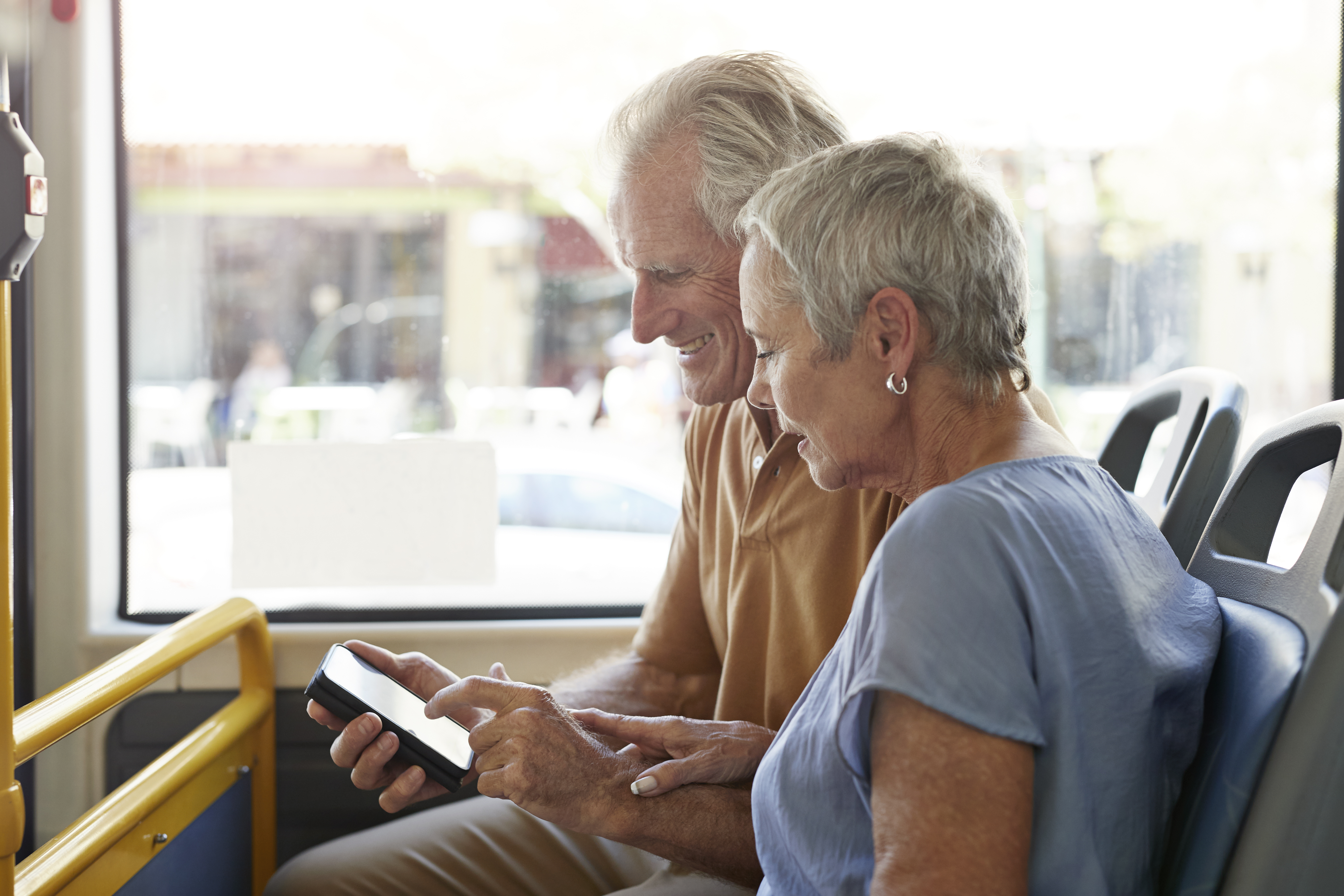 Senior couple, looking together at smartphone, while riding public bus