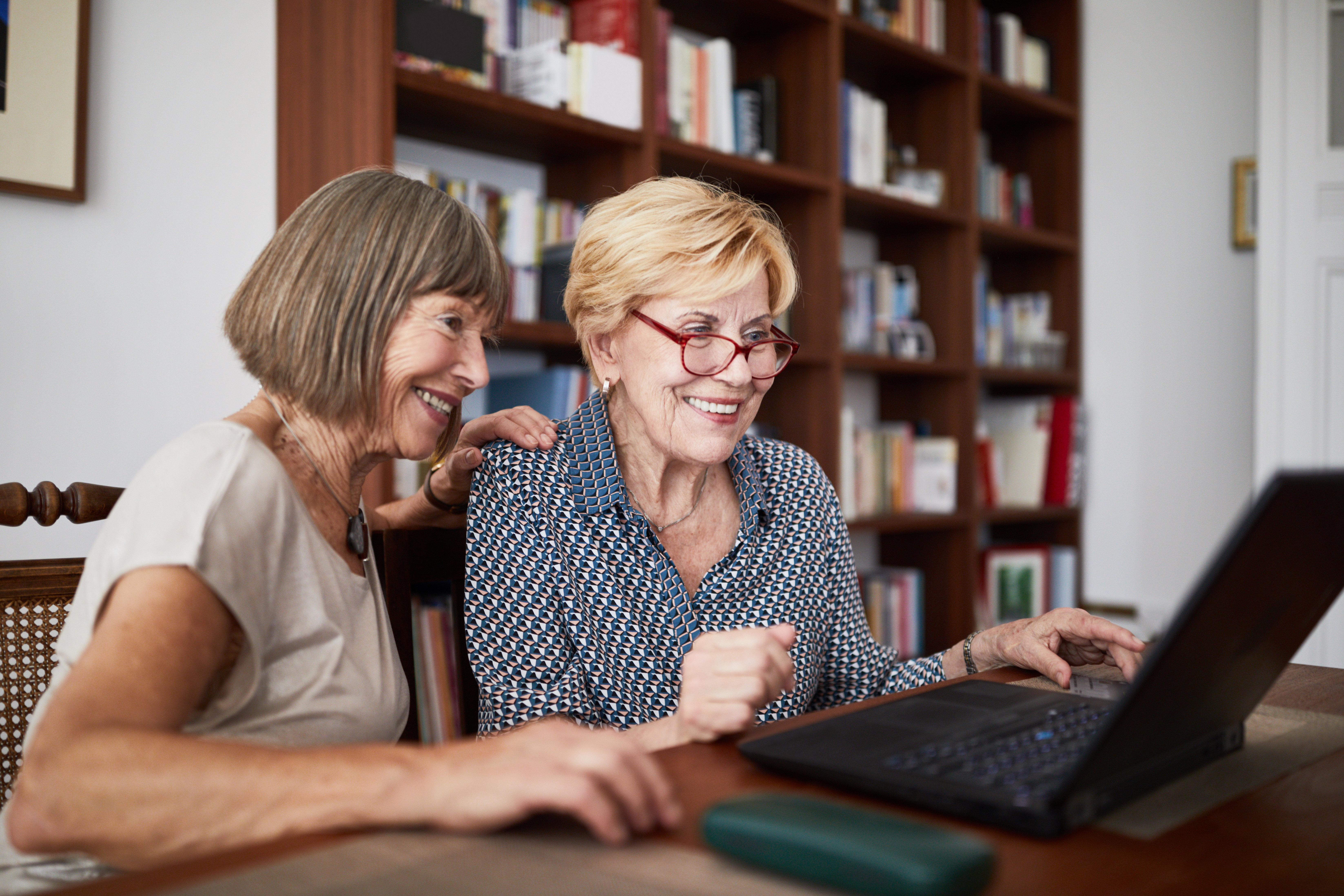 Two women sitting near one another at a table using laptop computer