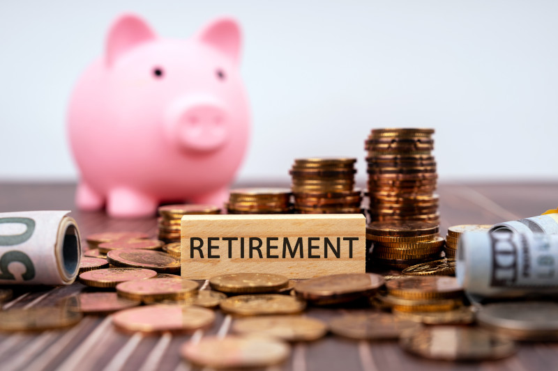 Pink piggy bank with dollars and coins behind a small wooden block that says Retirement