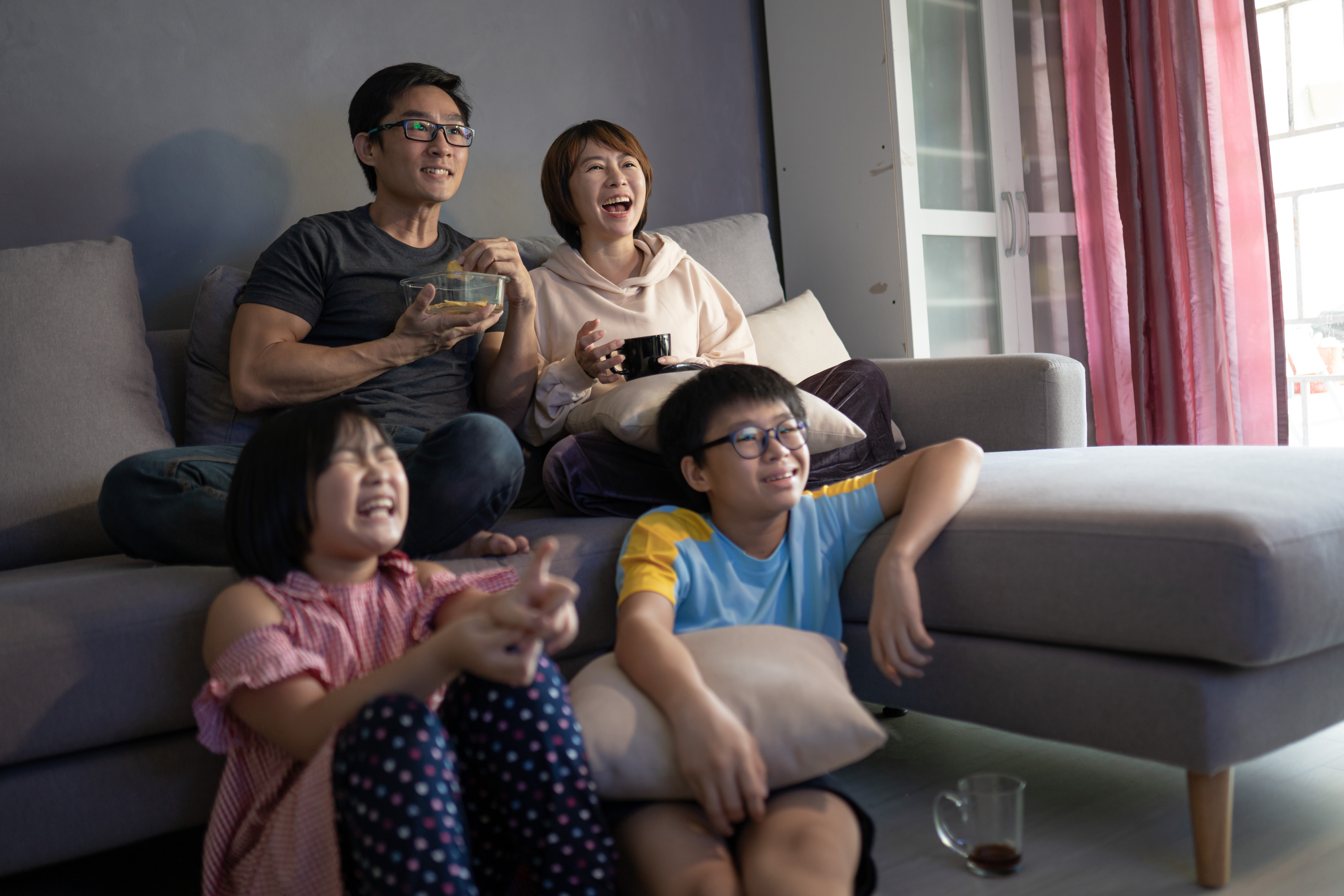 Asian Chinese family sitting on sofa watching television at home together.