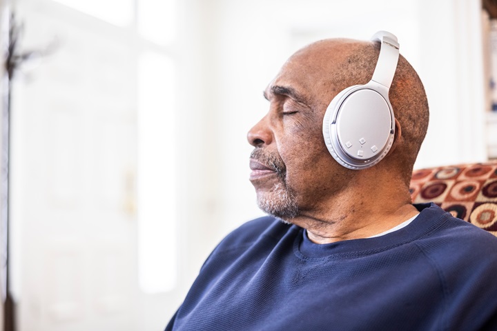 Senior man listening to music on wireless headphones at home