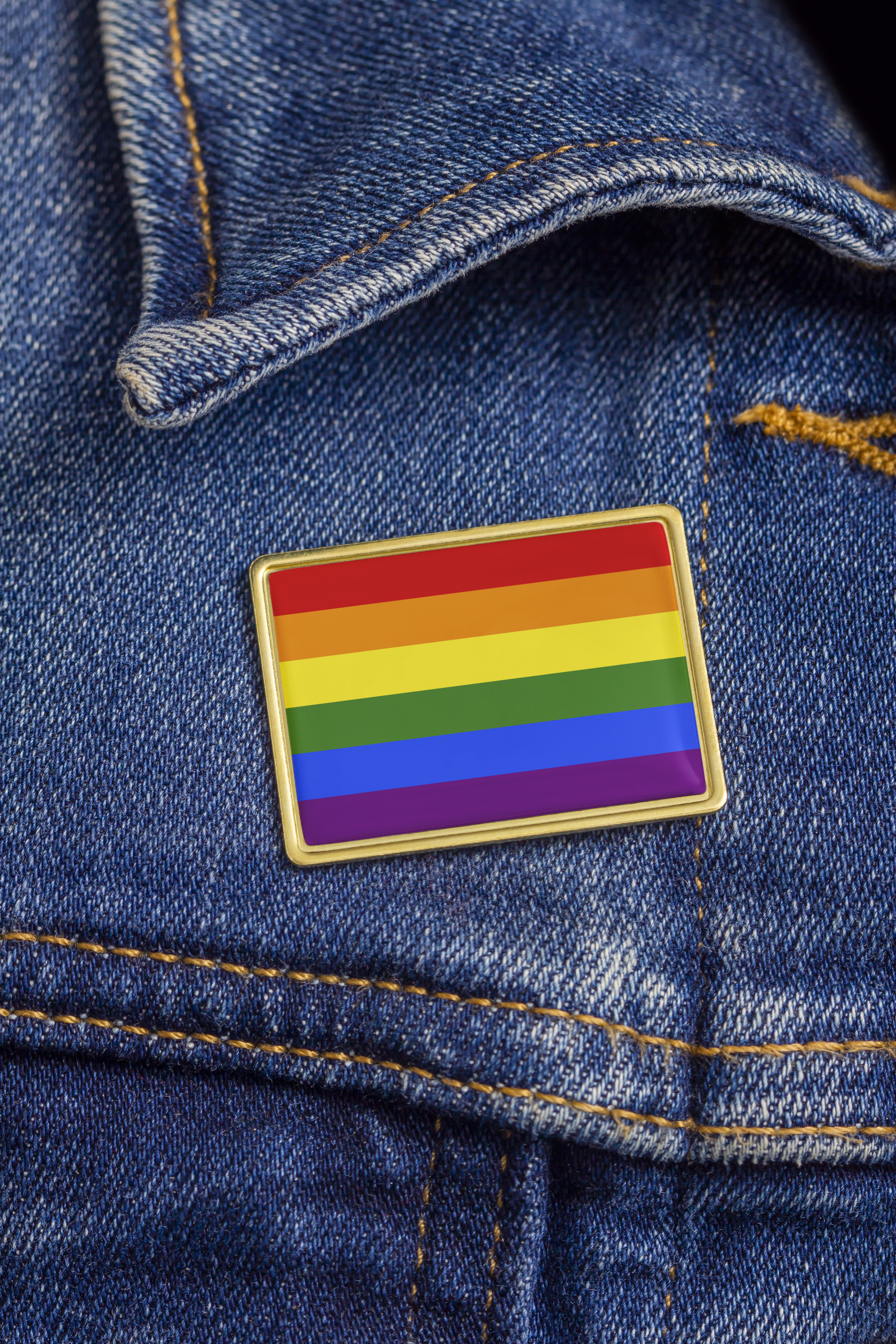 Gay pride flag pin on a denim jacket for LGBTQ identity, pride, and activism. The flag design is public domain for all uses.