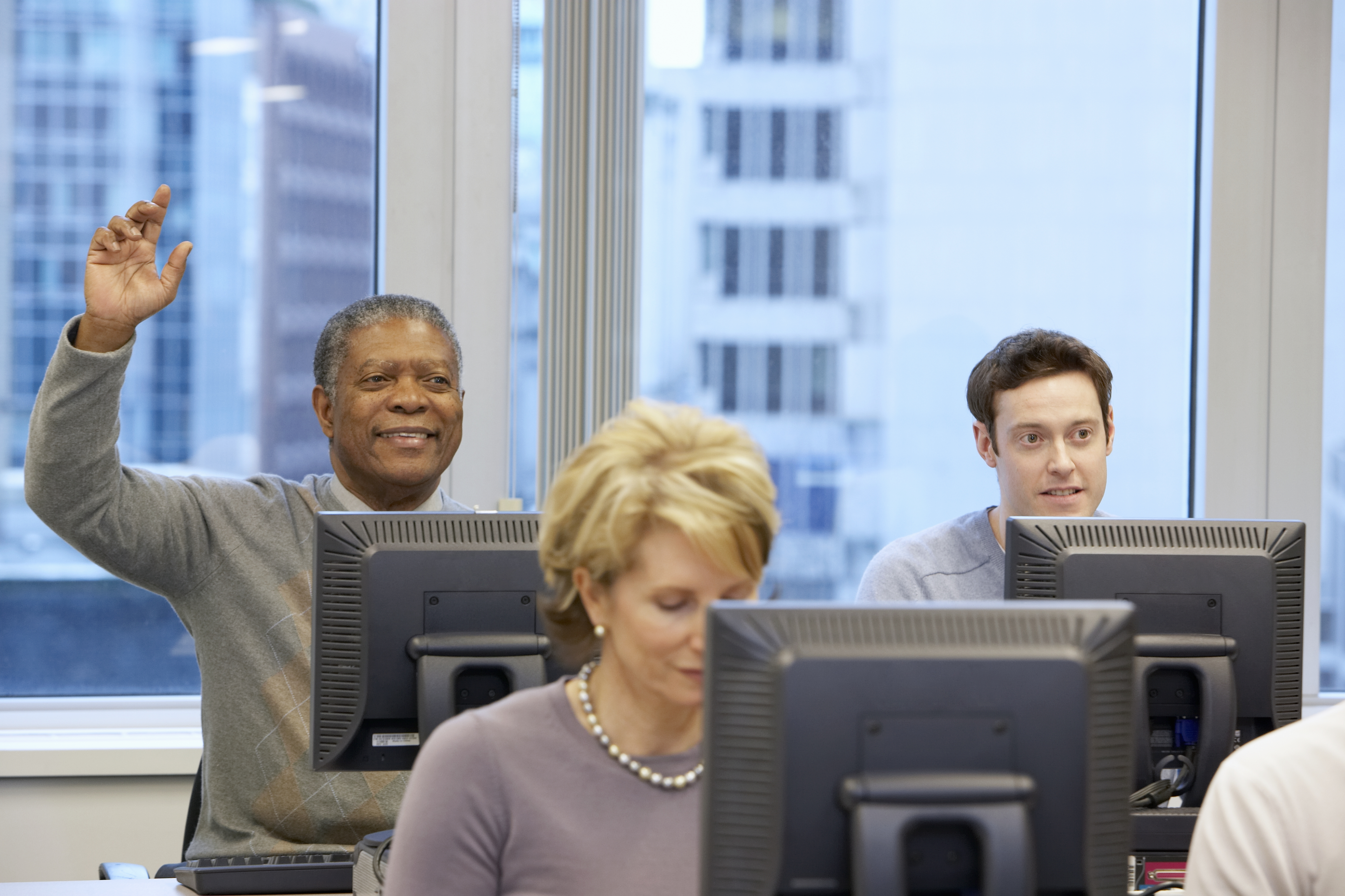 Group of people sitting at computers in office, one raising hand, front view