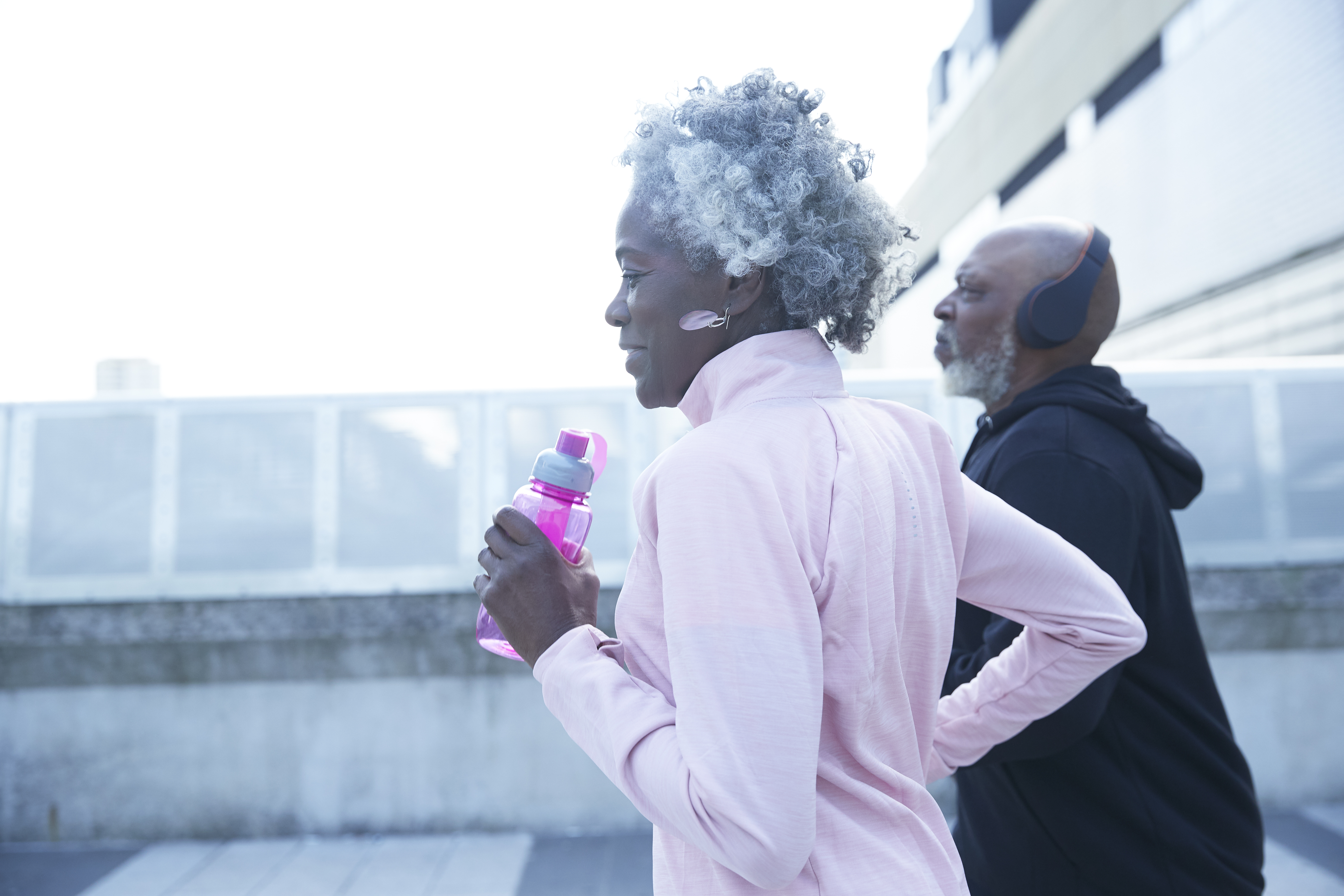 Senior woman holding water bottle while running with mature man