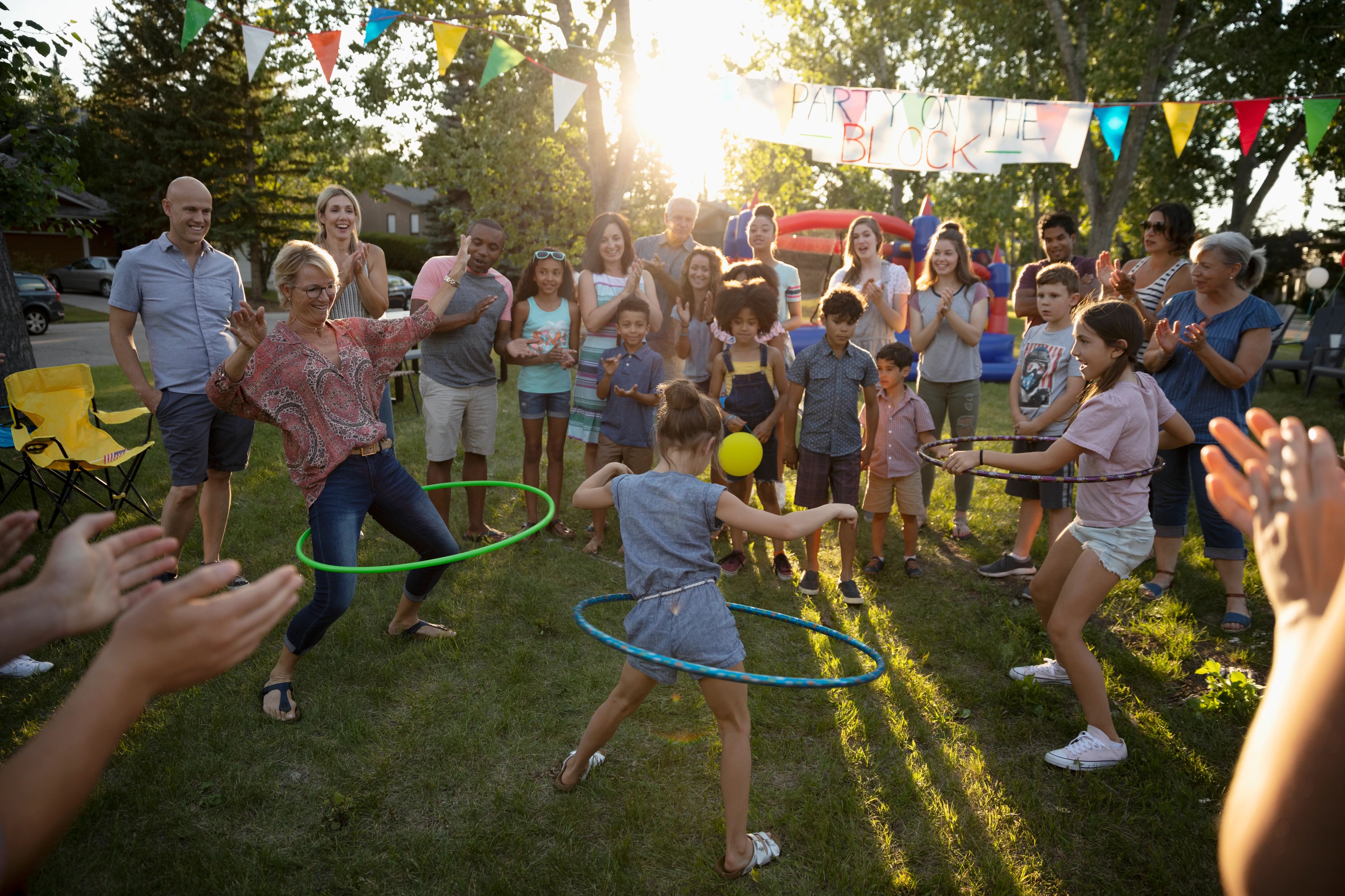 A diverse group of people, ranging in age,  play backyard games, including hula hooping. 