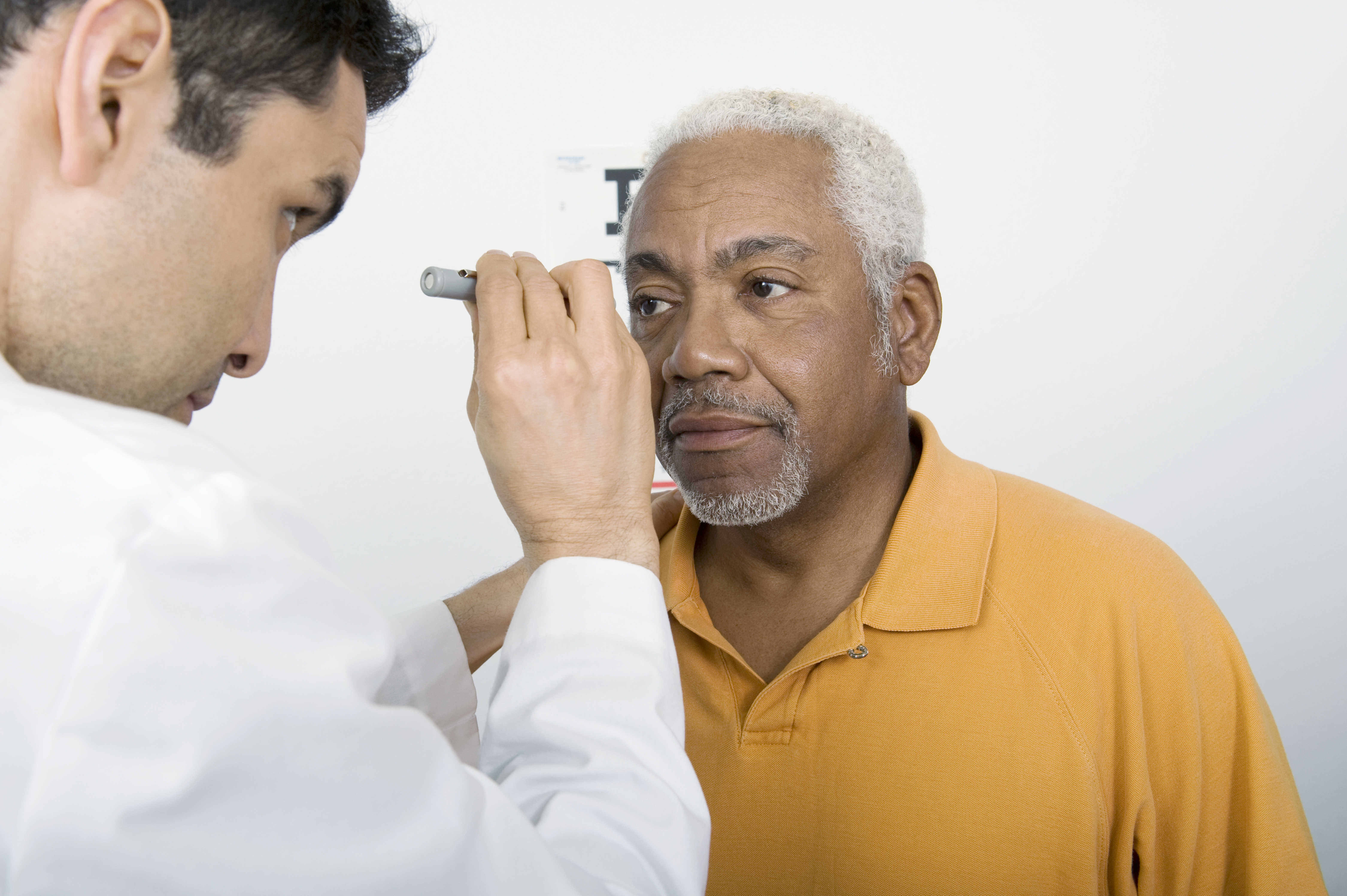 Mid adult doctor examines senior man's eyesight