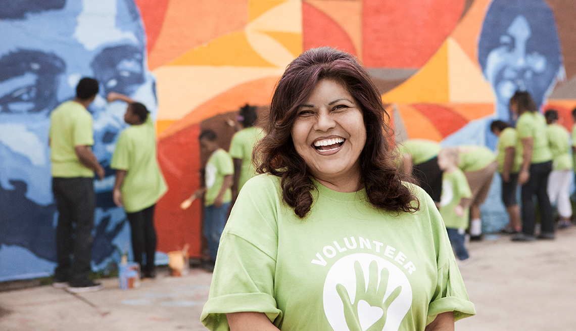 A woman smiles while a group of community volunteers paint a wal