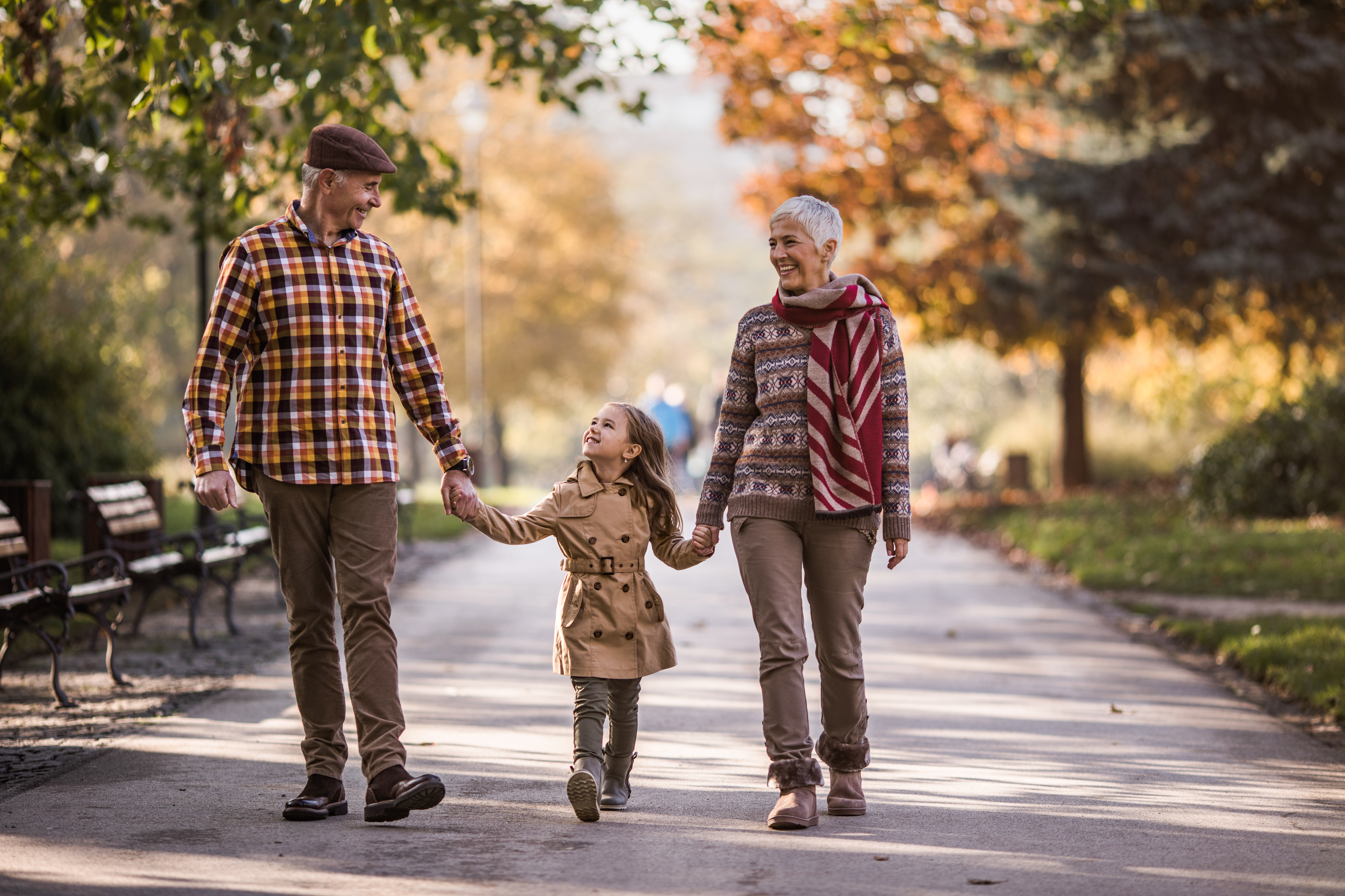 Happy grandparents and their small granddaughter taking a walk in autumn day.