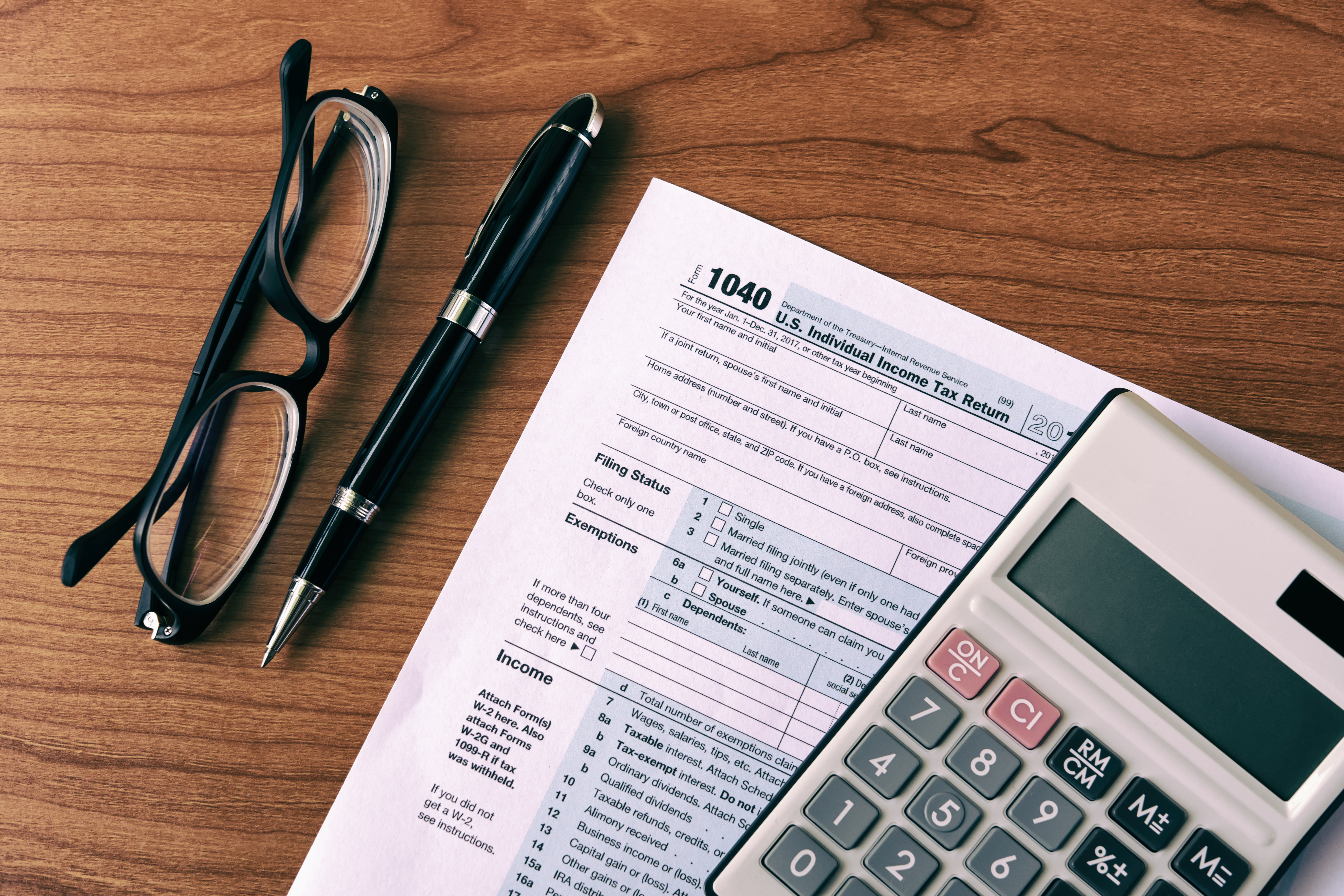 1040 tax document with a calculator on top and glasses and a pen on a table