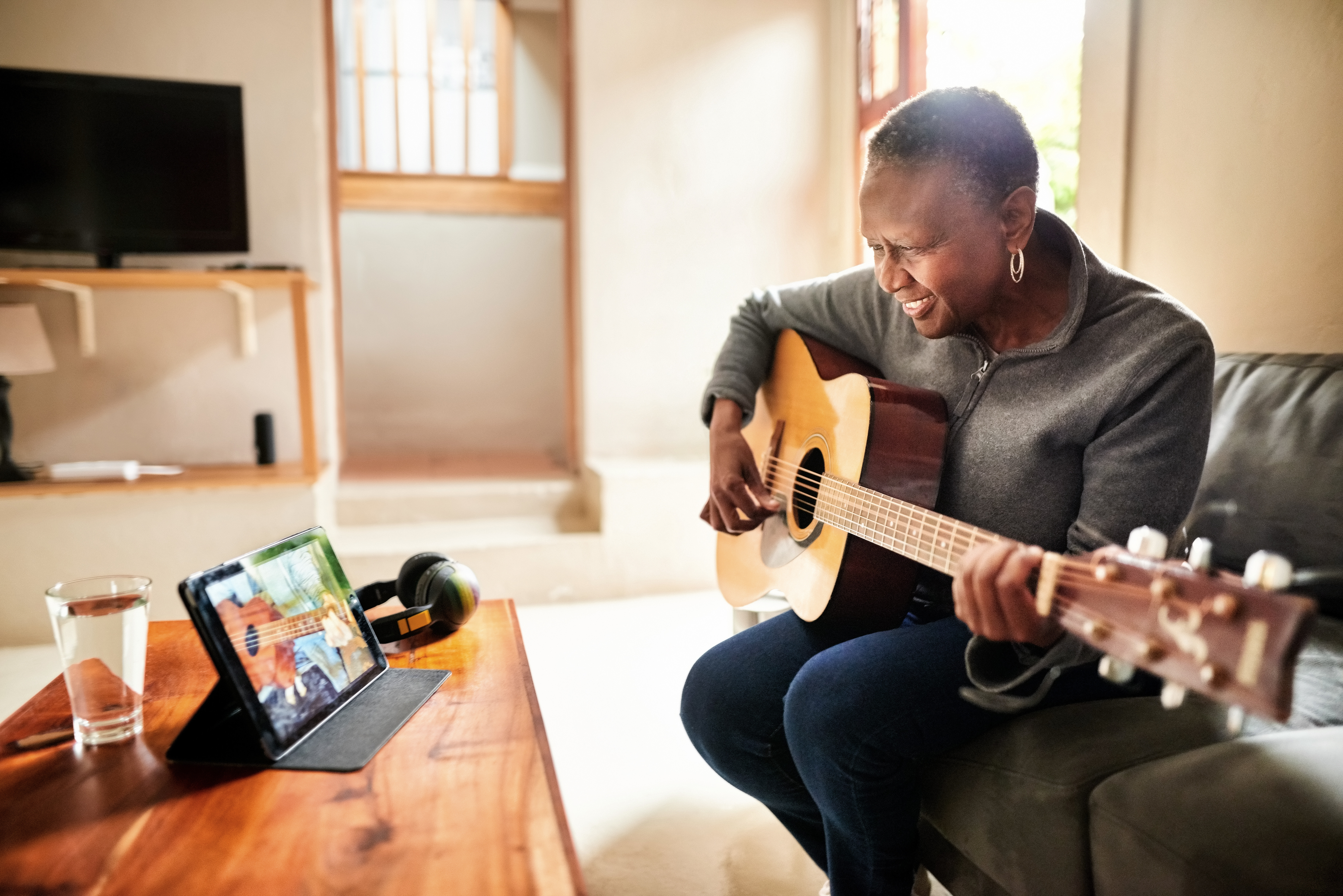 Senior woman learning guitar online with a digital tablet