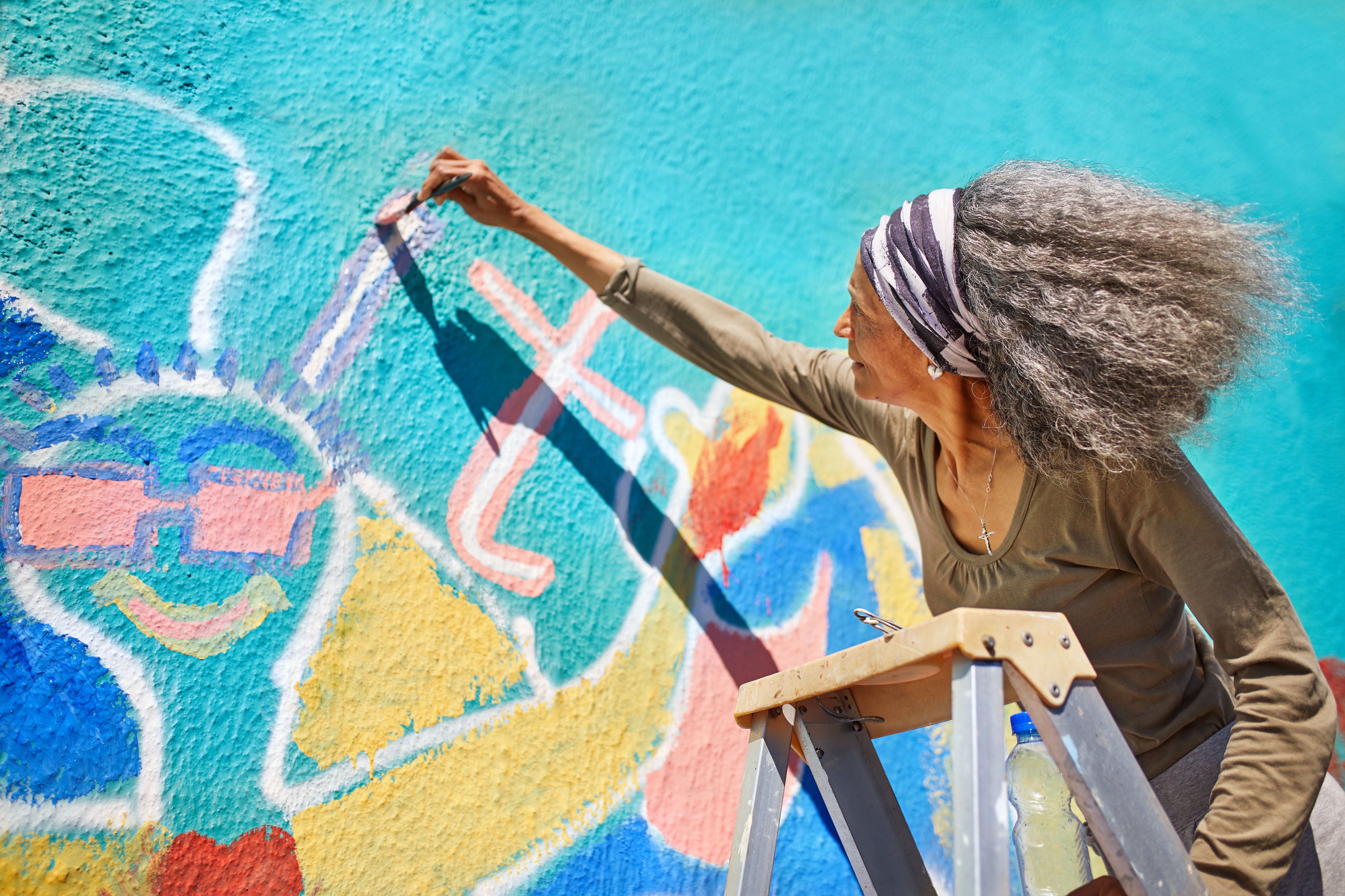 Senior woman painting vibrant mural on sunny wall