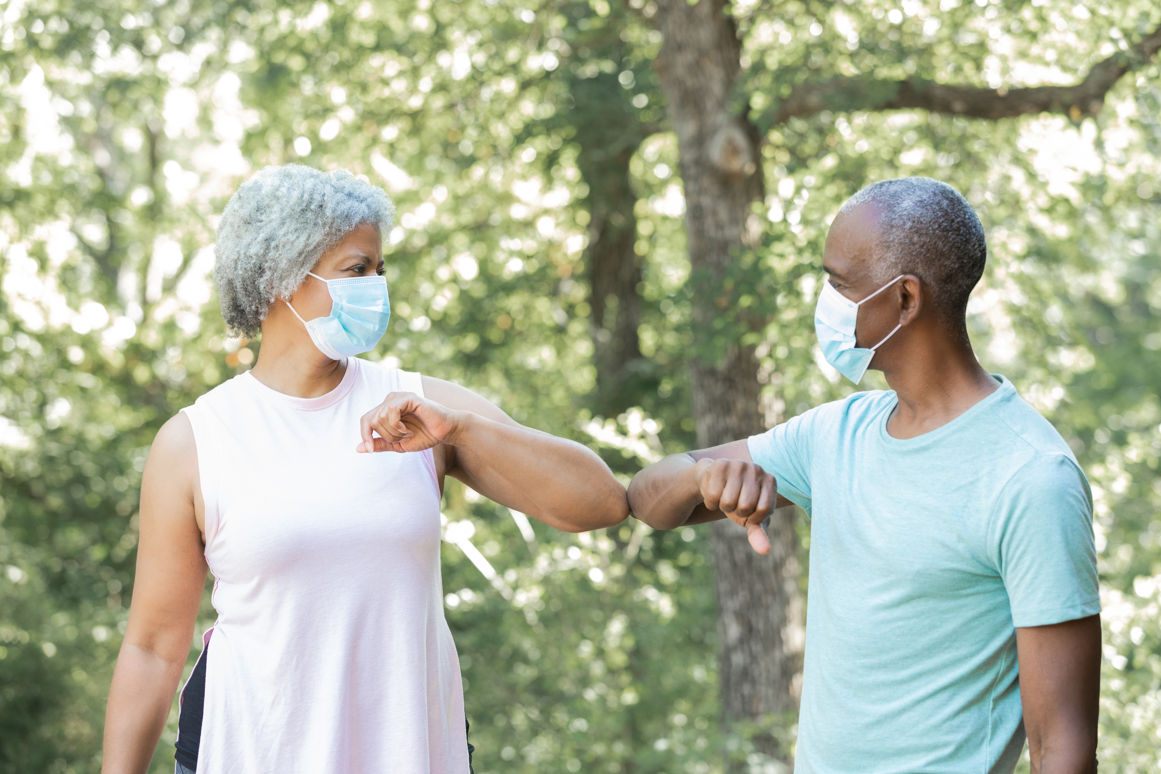 Senior man and woman wearing masks greet each other by touching elbows instead of shaking hands