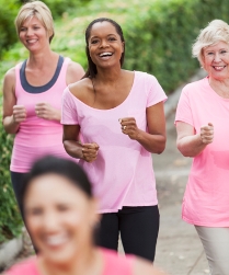 Multi-ethnic group of women (30s, 40s, 60s) wearing pink, participating in breast cancer rally.  Focus on African American woman (40s) in middle.