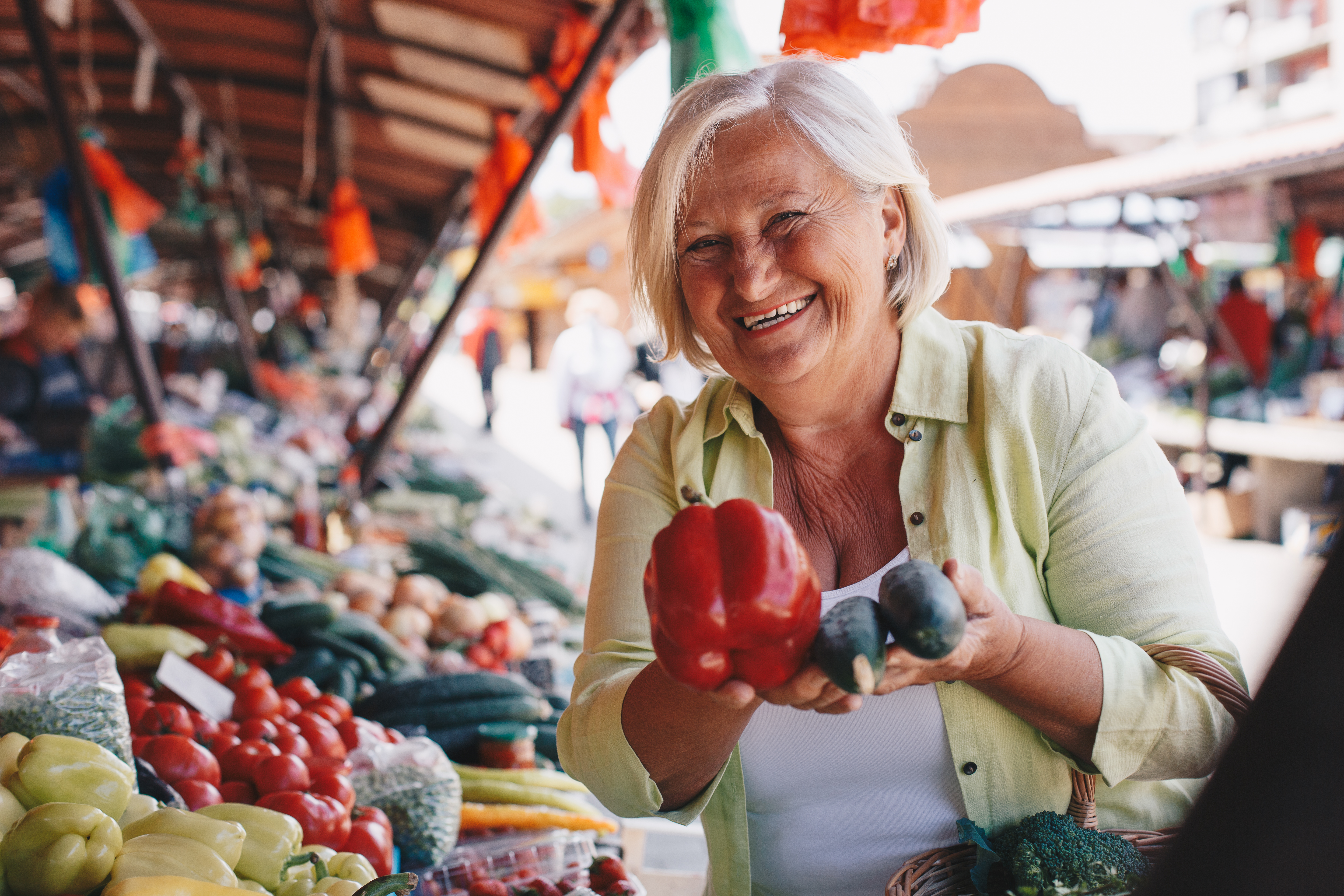 Senior woman holding red bell pepper and cucumbers.