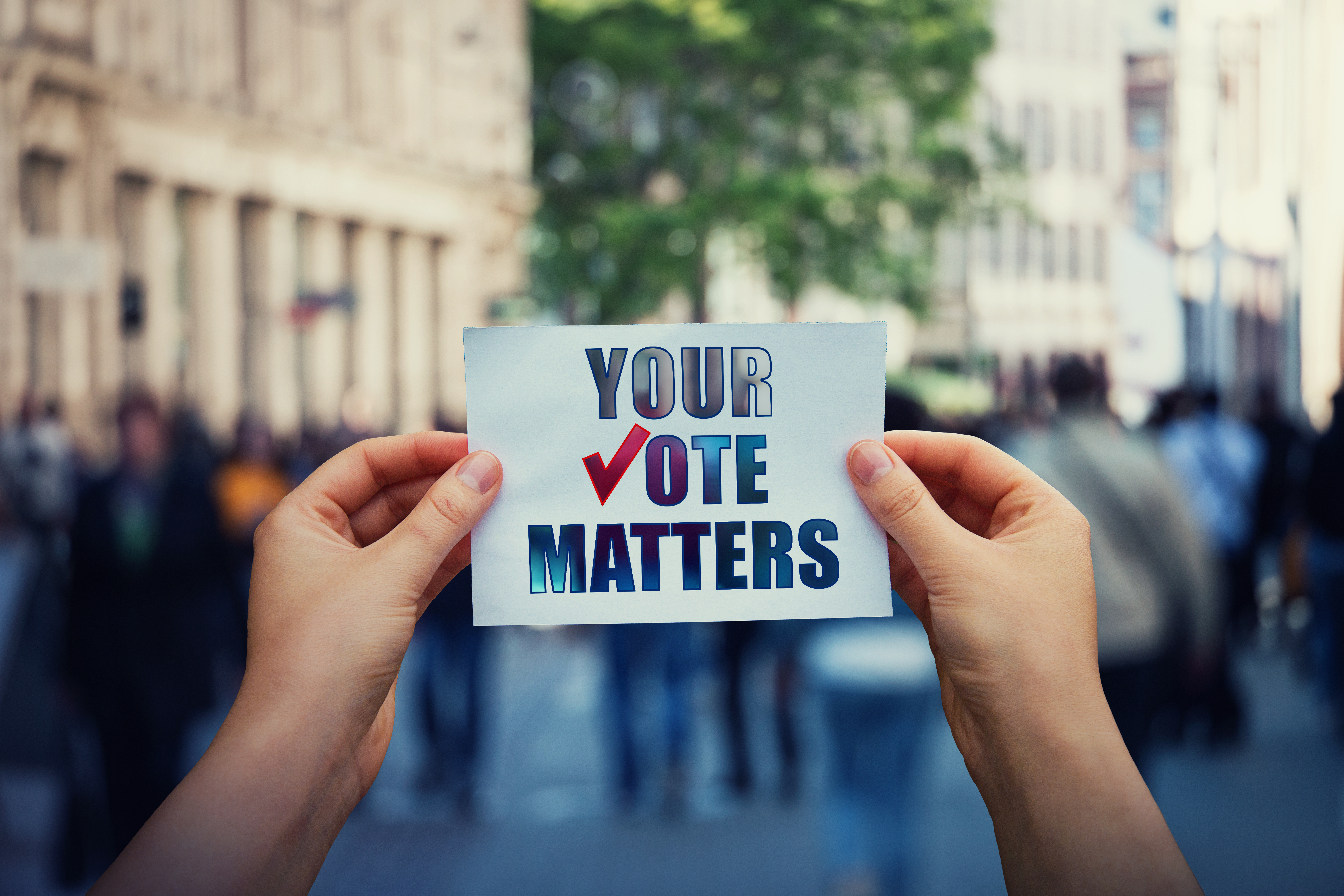 Hands hold a paper sheet with the message your vote matters over a crowded street background. People legal and democratic rights, every voice counts. Election campaign and electoral agitation concept