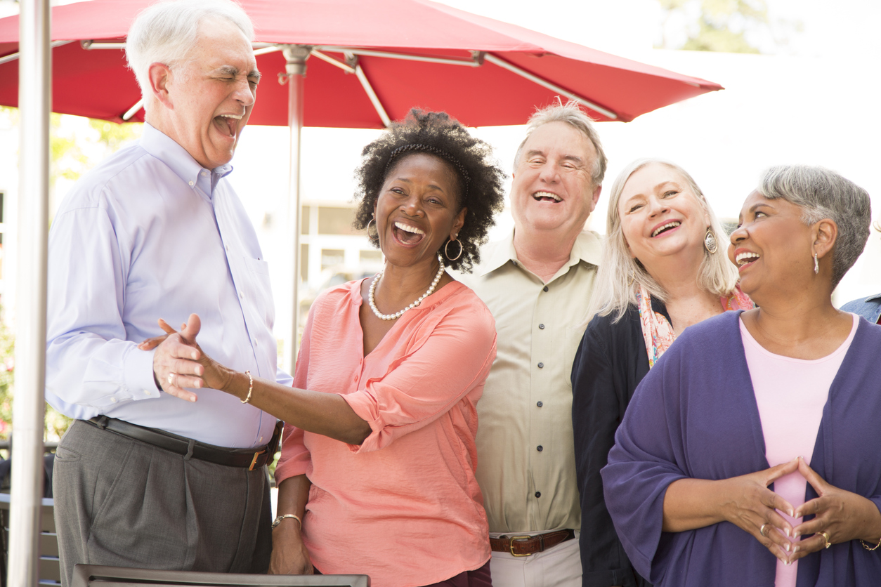 Multi-ethnic group of senior adult friends enjoy visiting at outdoor cafe.