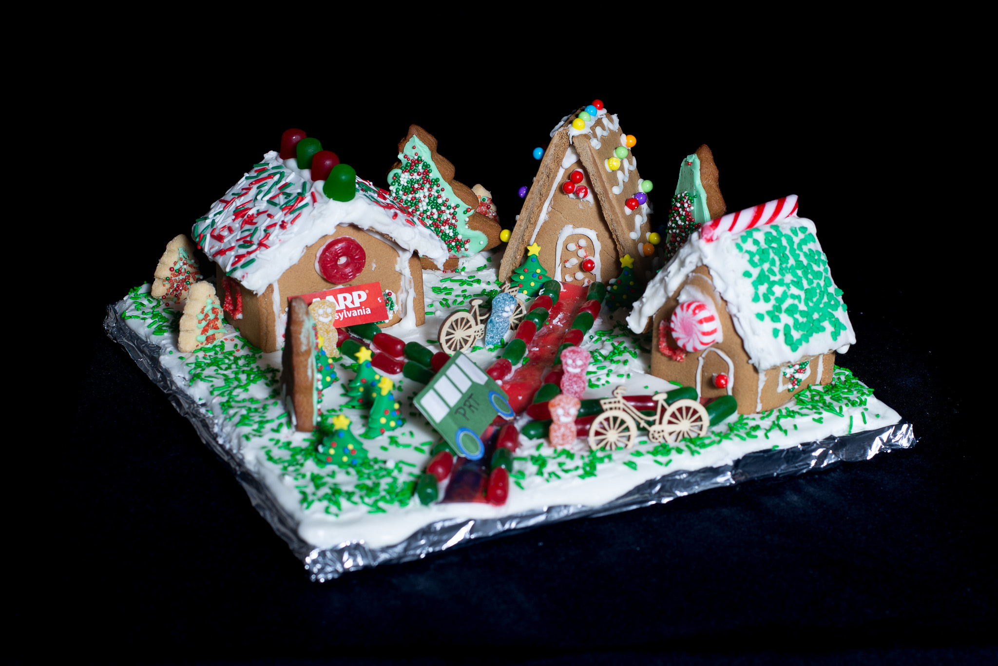 Three gingerbread houses connected with a walkway, displaying bikes and a bus. 