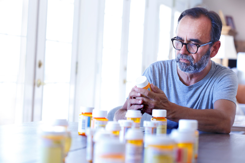 Latino Man Sitting At Table Sorting Through Prescrption Medications