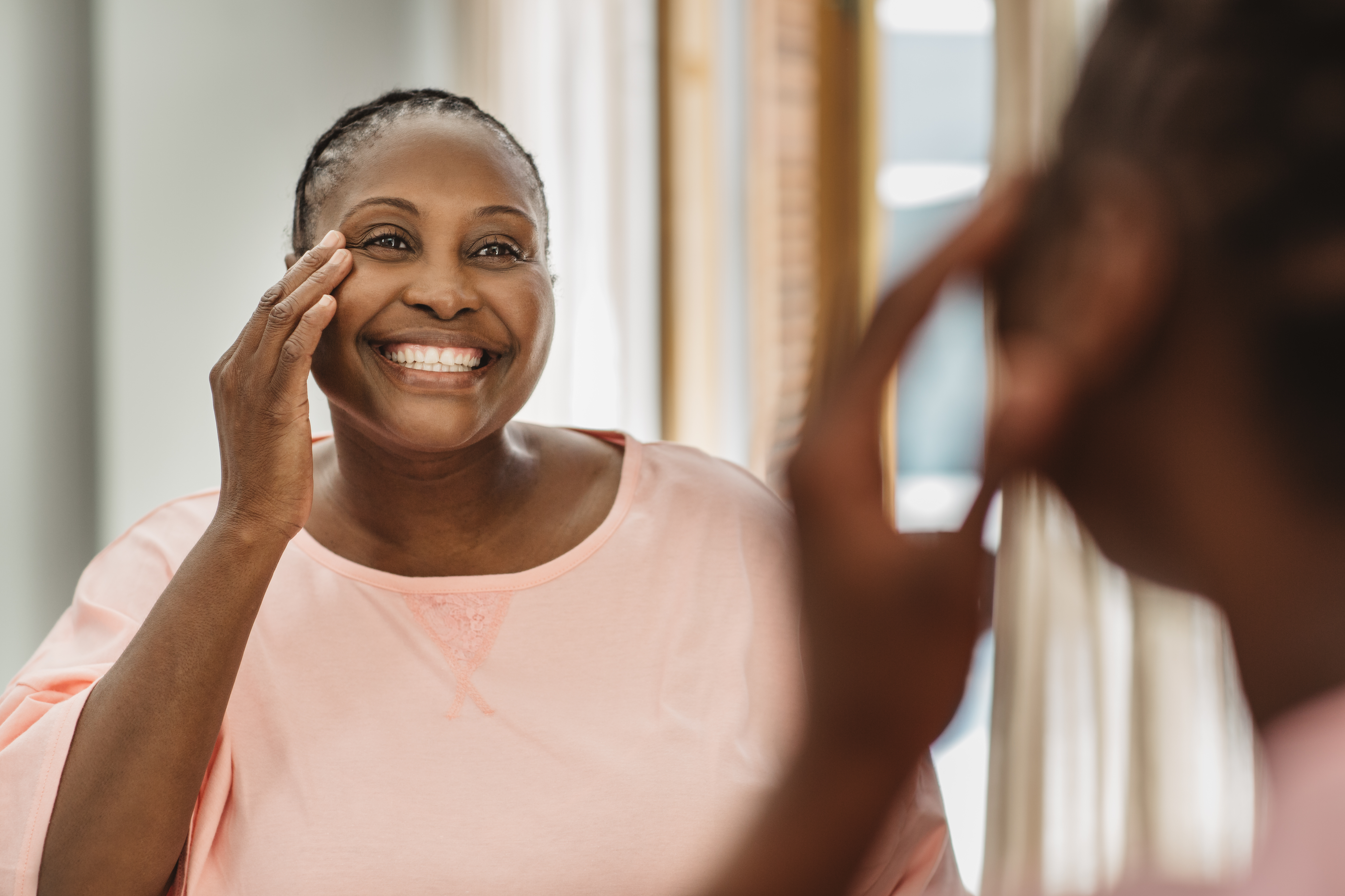 Smiling African American woman examining her skin in the bathroom