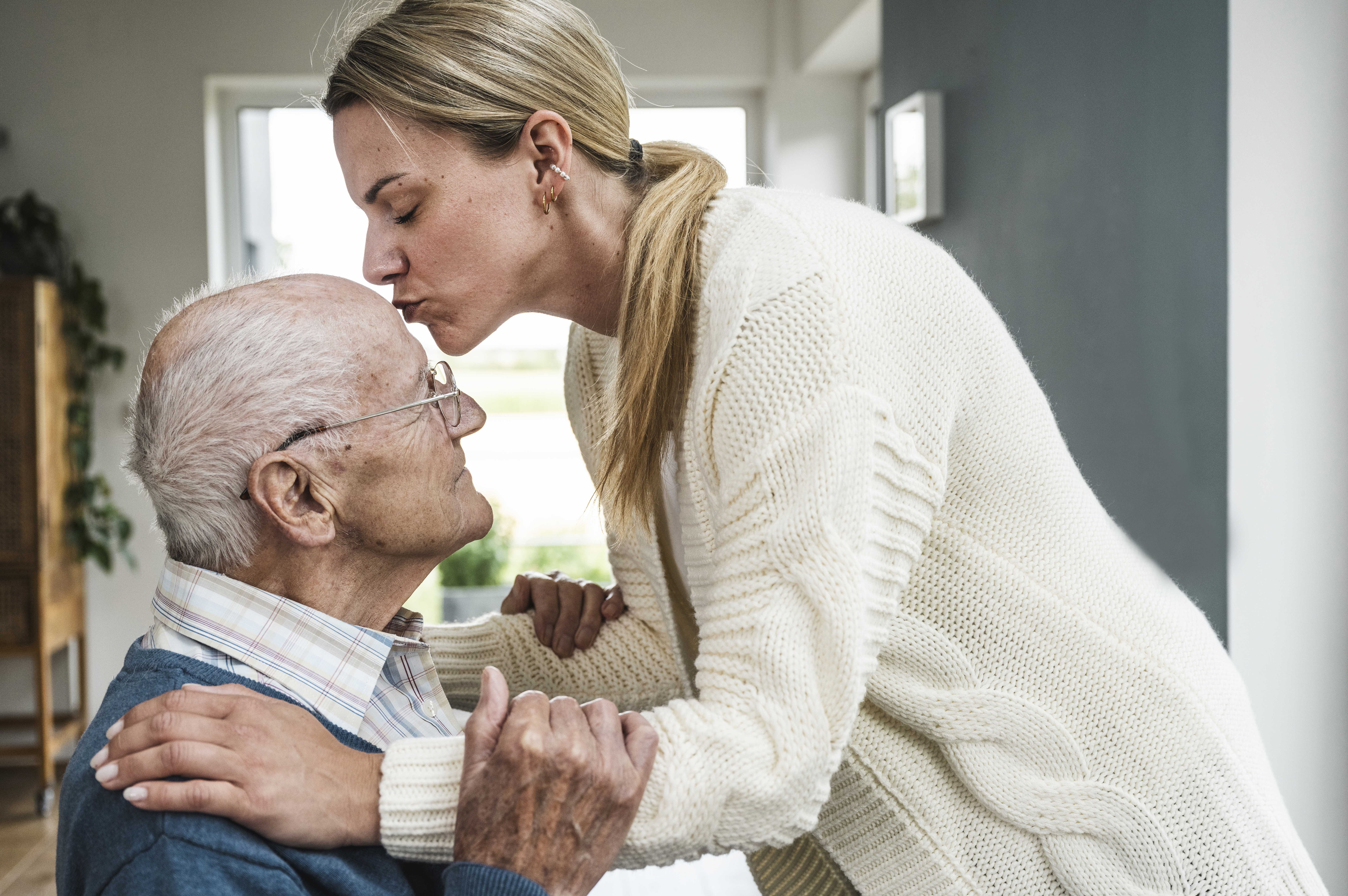 Blond woman kissing father on head at home