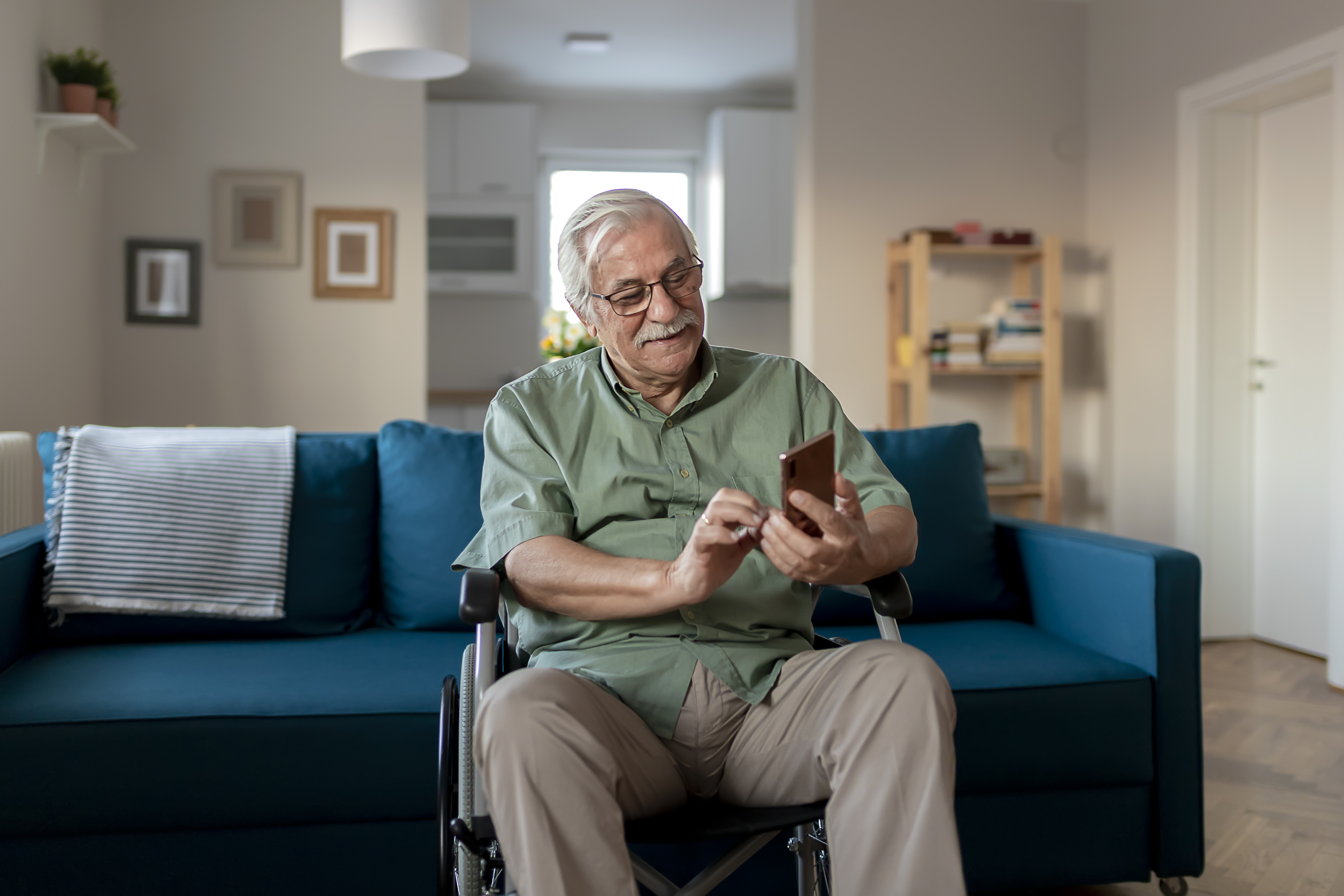 Handicapped Senior Man Sitting in a Wheelchair and Using a Smartphone