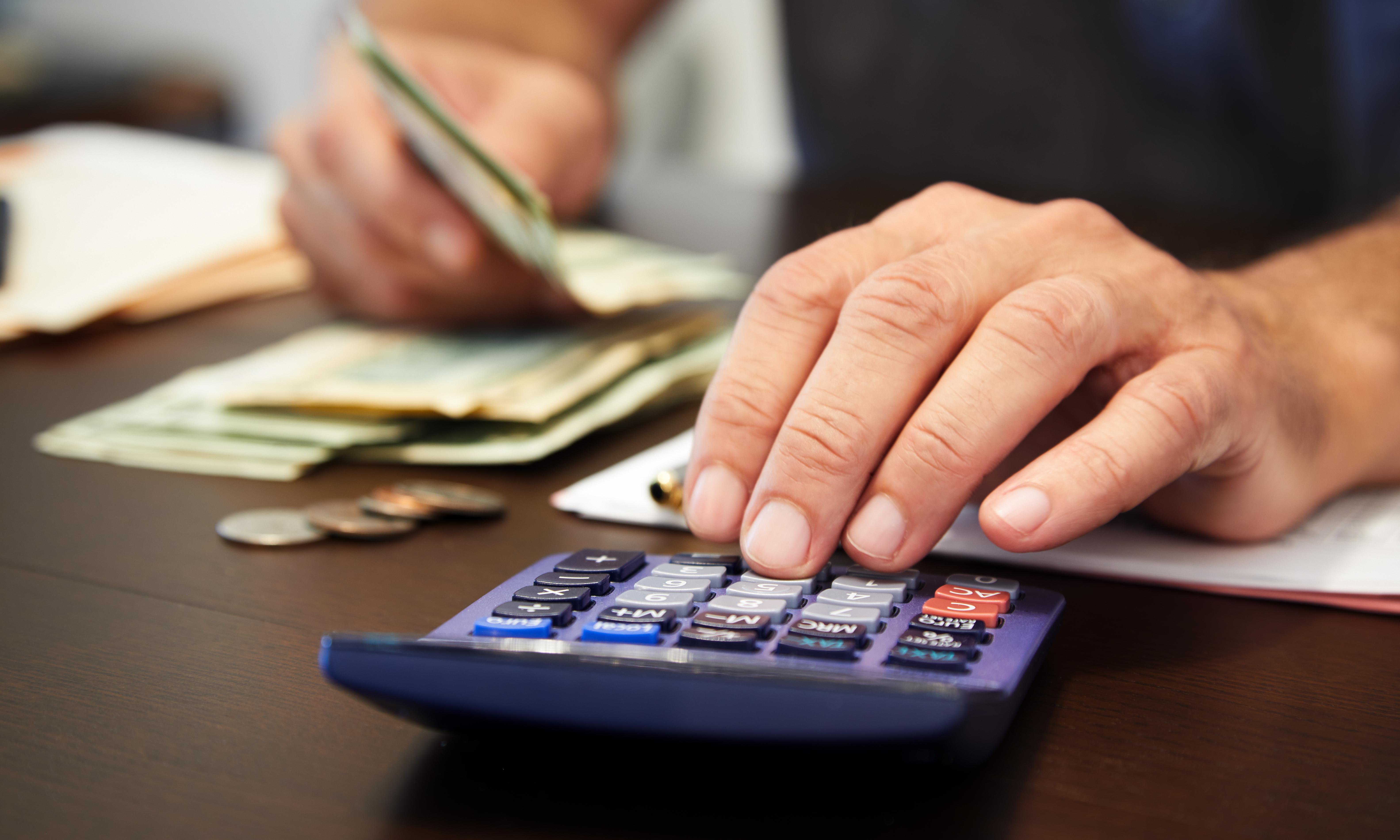 Close-up of a person's hand using a calculator and counting money