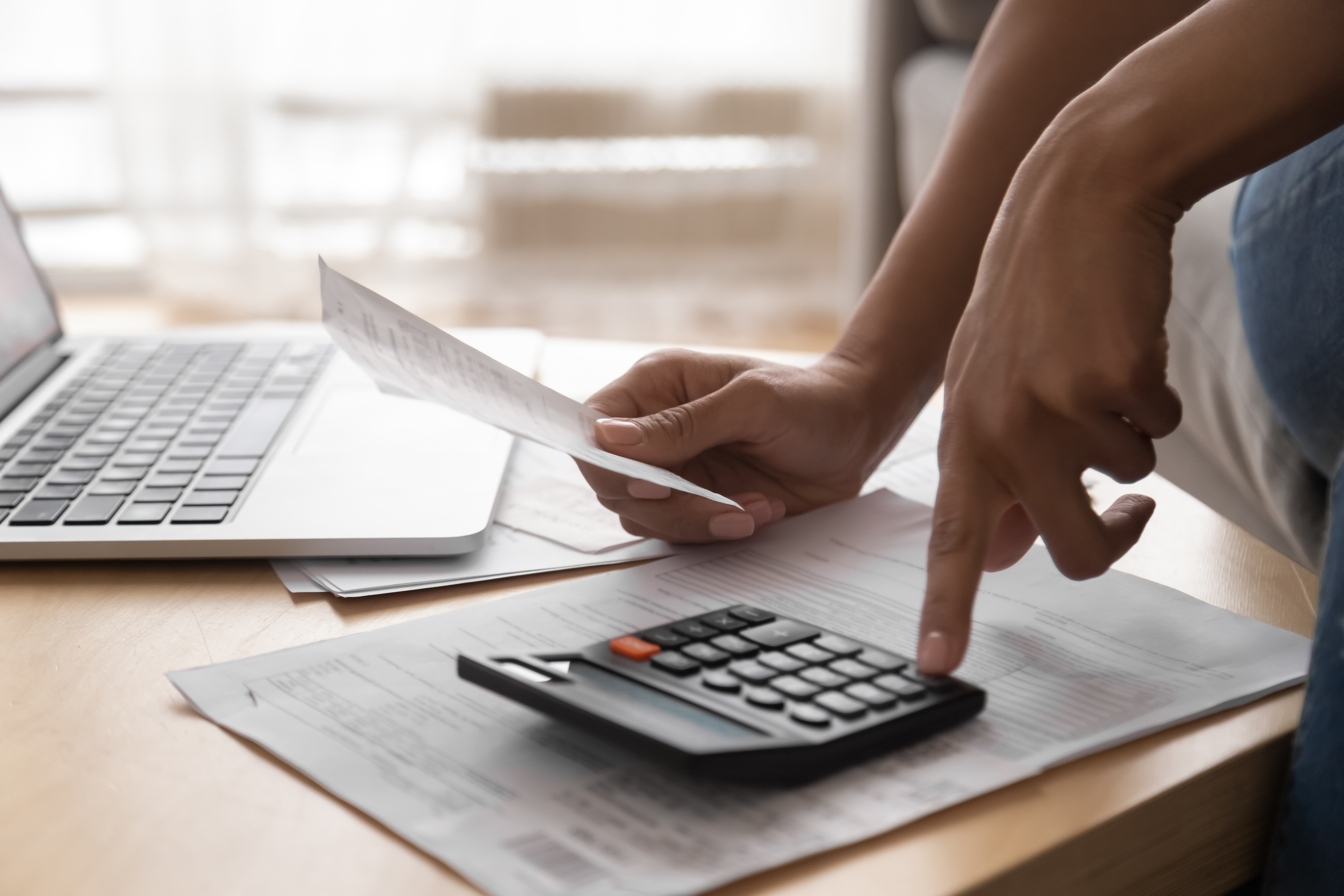 African woman holding paper bills using calculator, close up view