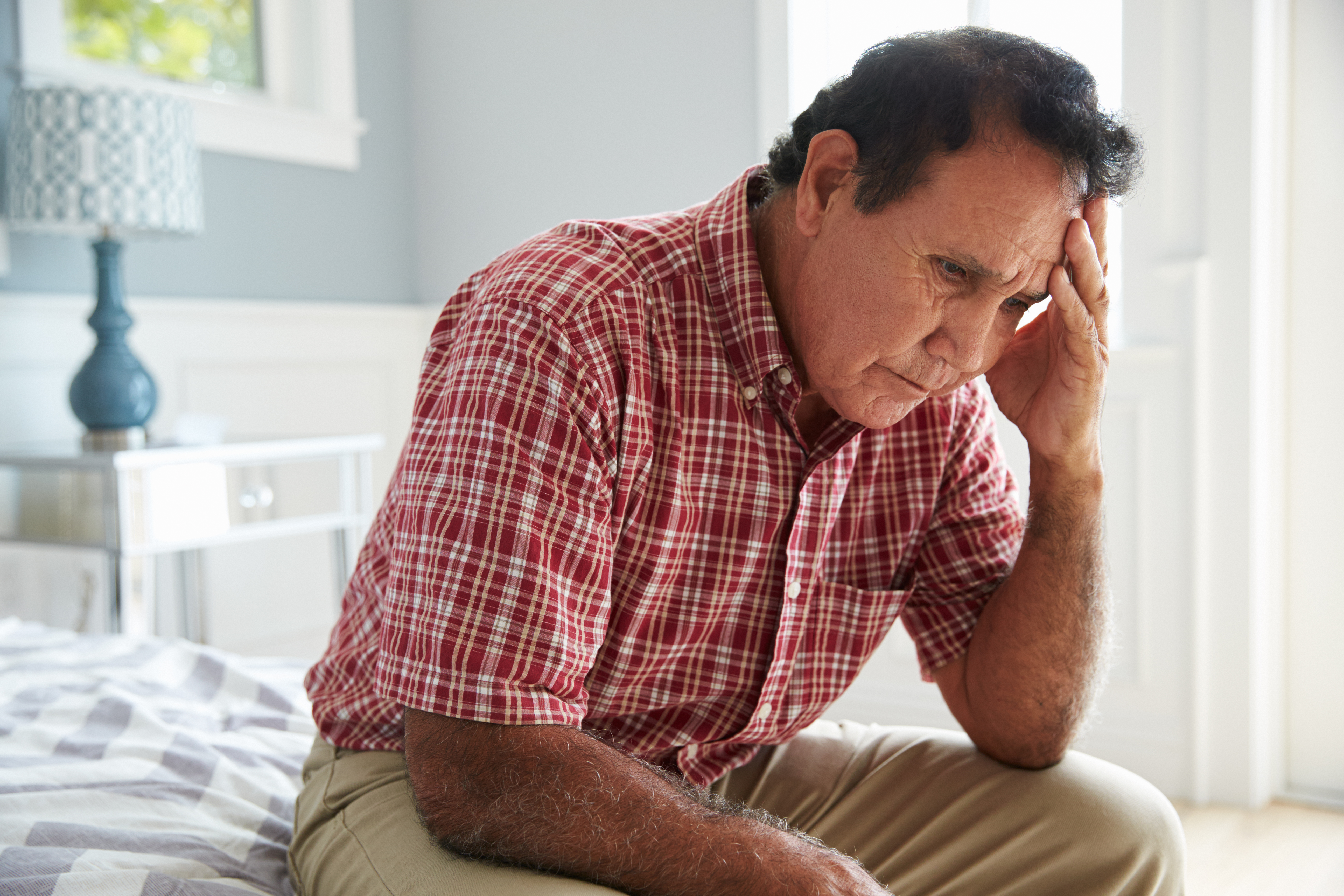 Senior Hispanic Man Sitting On Bed Suffering With Depression