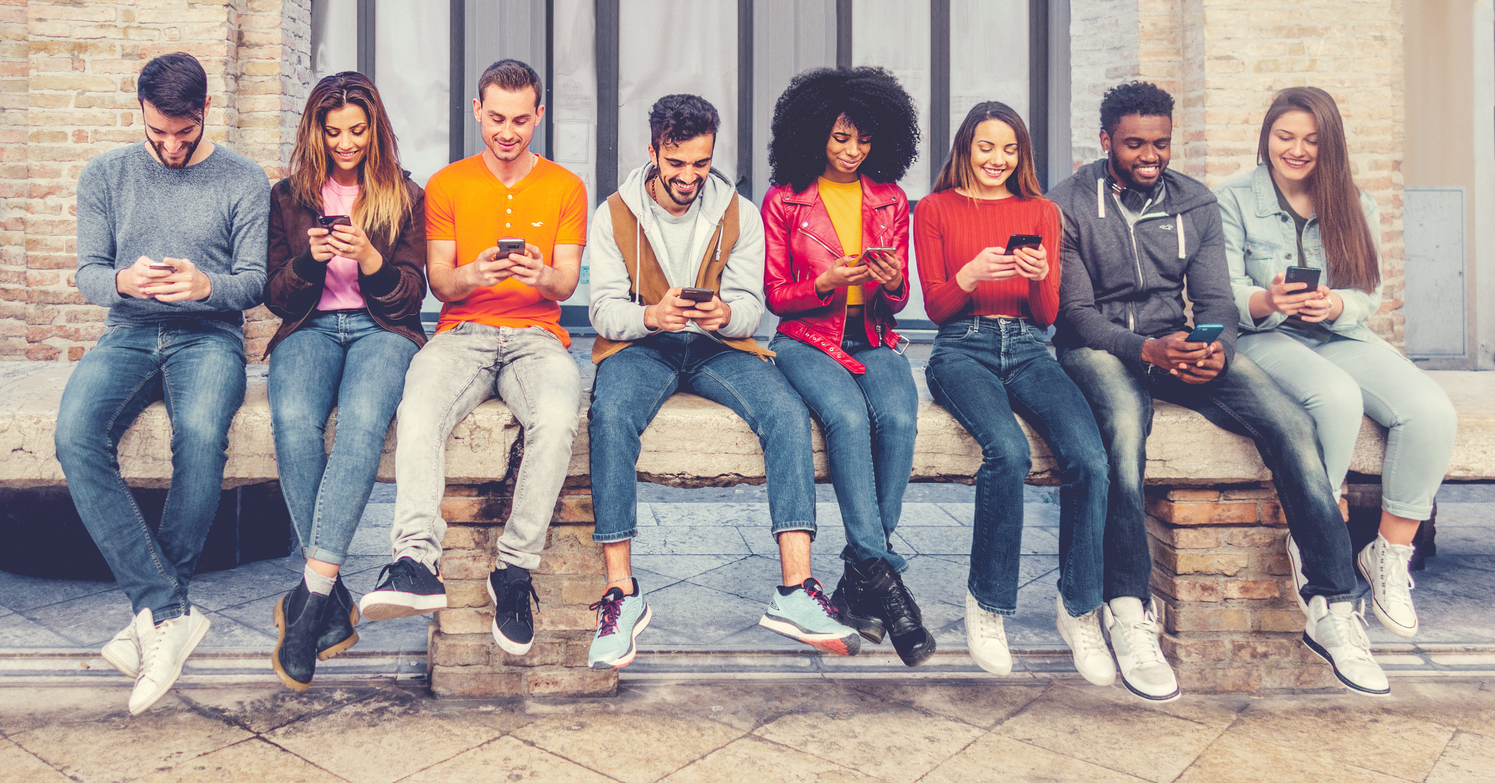 Group of multiracial young people sitting outdoors and watching down to his smartphones