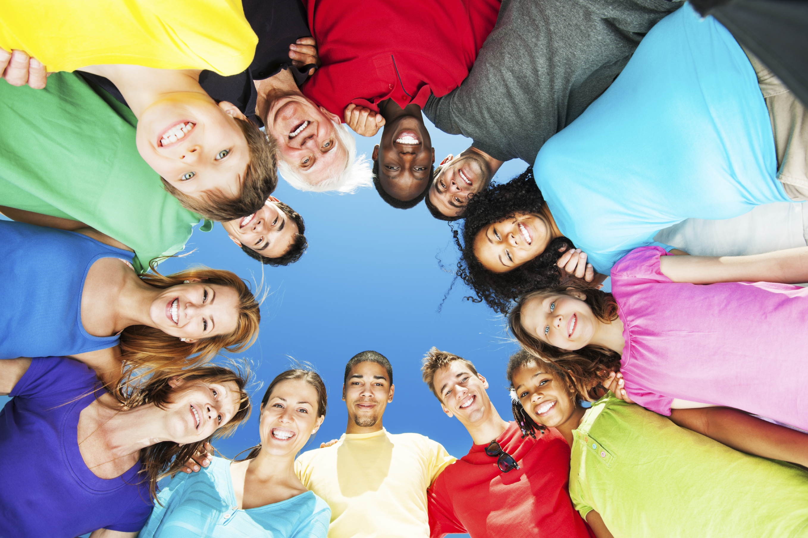 Group of embraced people standing in circle against blue sky.