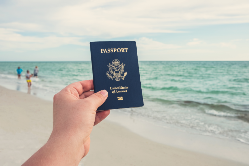 A person holding a passport on a beach.