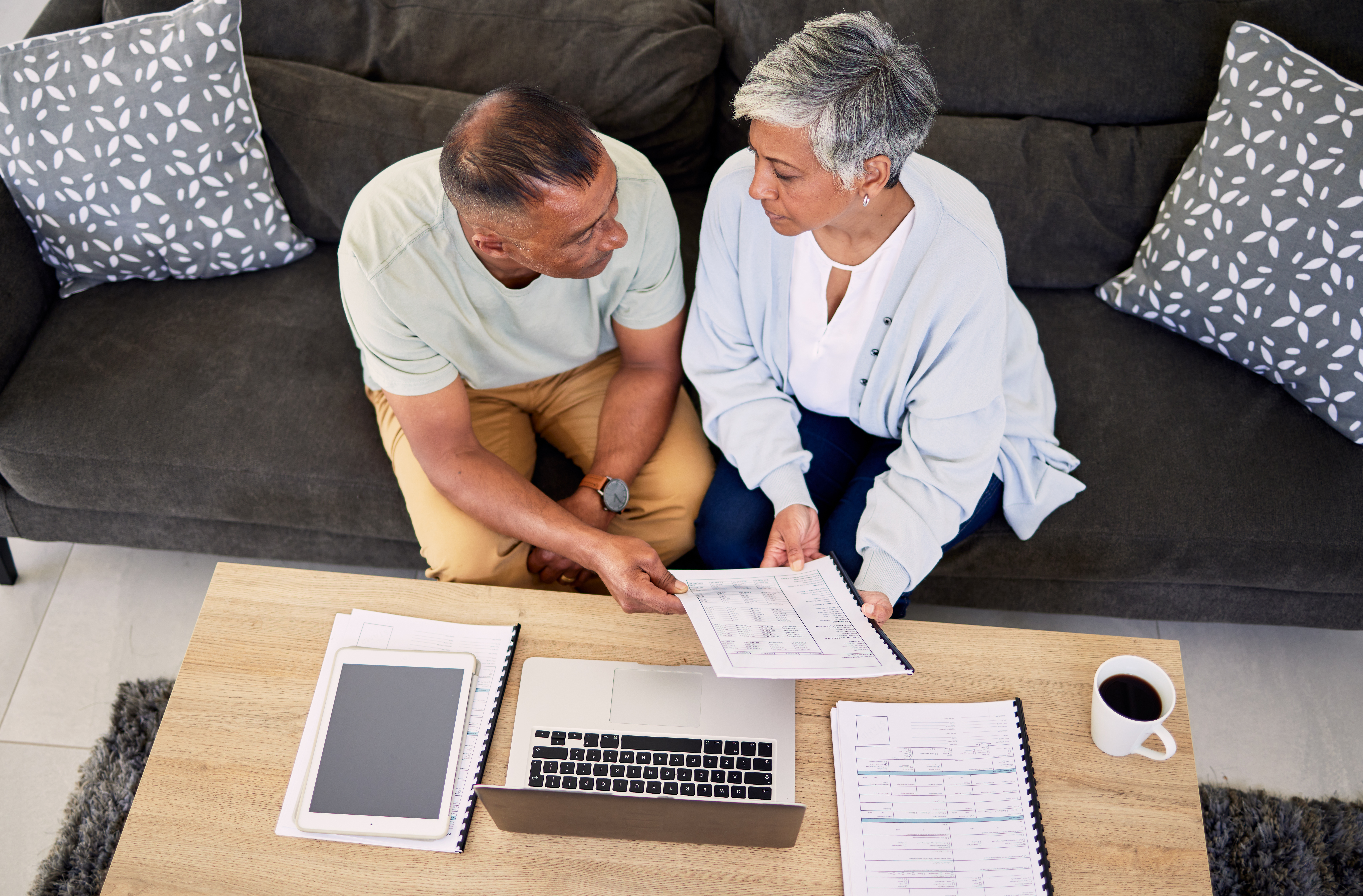 Senior couple, tax documents and laptop in home living room for discussion, planning and finance. Elderly man, old woman and paperwork for financial compliance in top view, lounge sofa and retirement