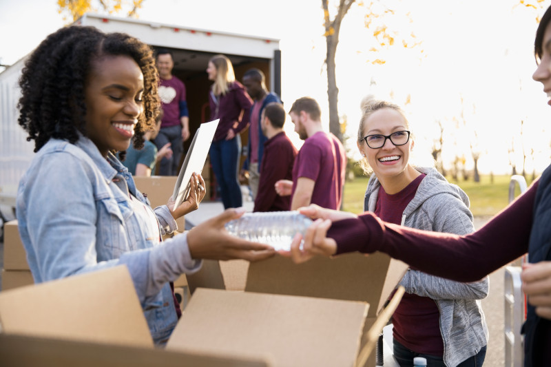 Smiling volunteers packing water bottles into cardboard boxes outside truck