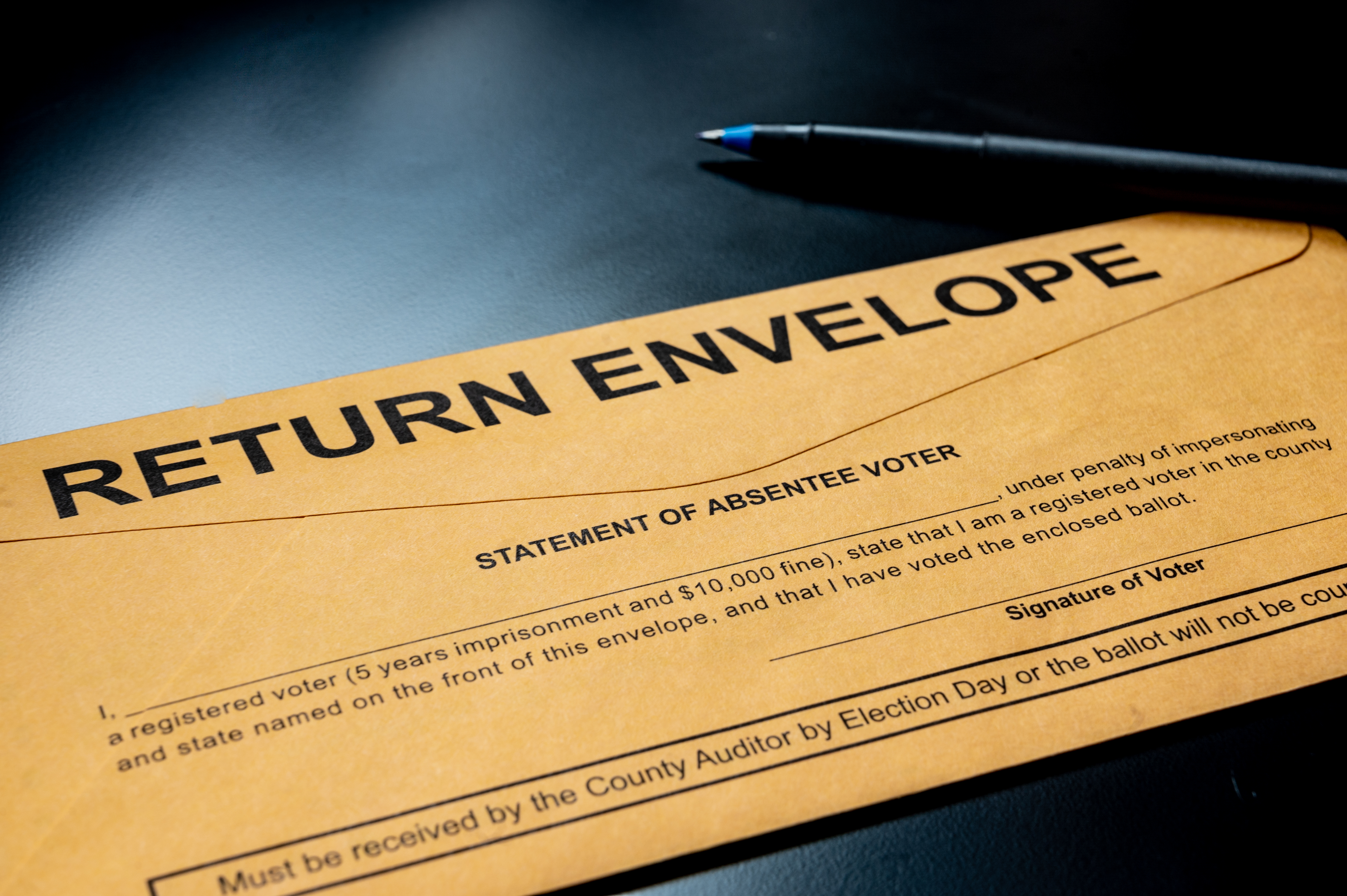 brown absentee ballot return envelope on a black desk with ink pen