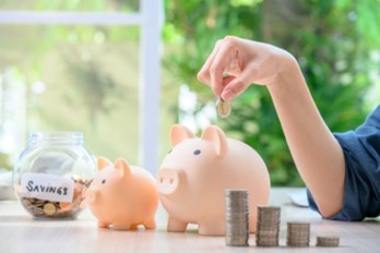 Woman's hand pictured dropping a coin into a piggy bank.