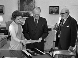 President Gerald R. Ford and First Lady Betty Ford looking at Ansel Adams' photographs in the Oval Office, with the photographer looking on. 