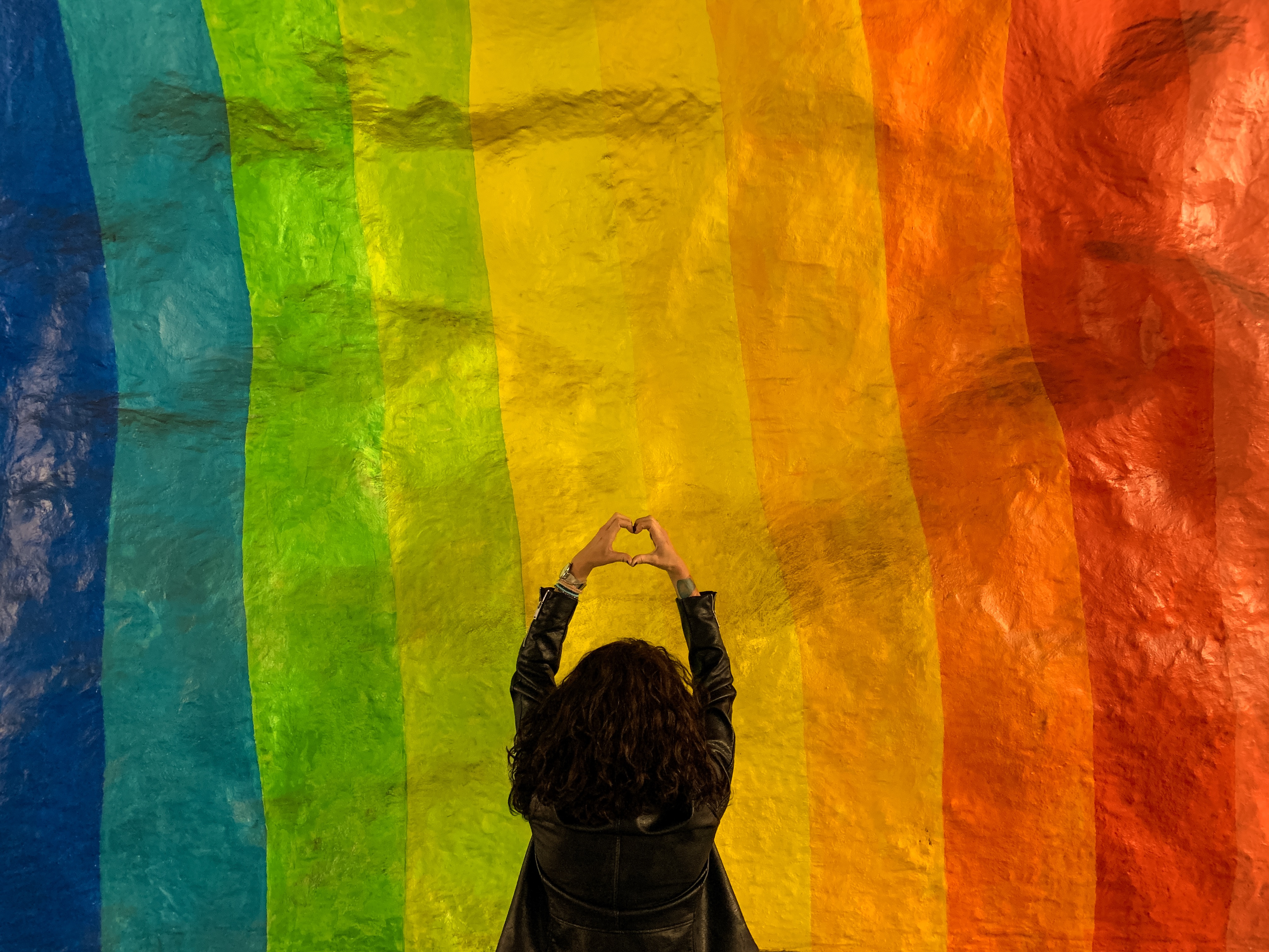 Rear View Of Woman Making Heart Shape While Standing Against Multi Colored Wall