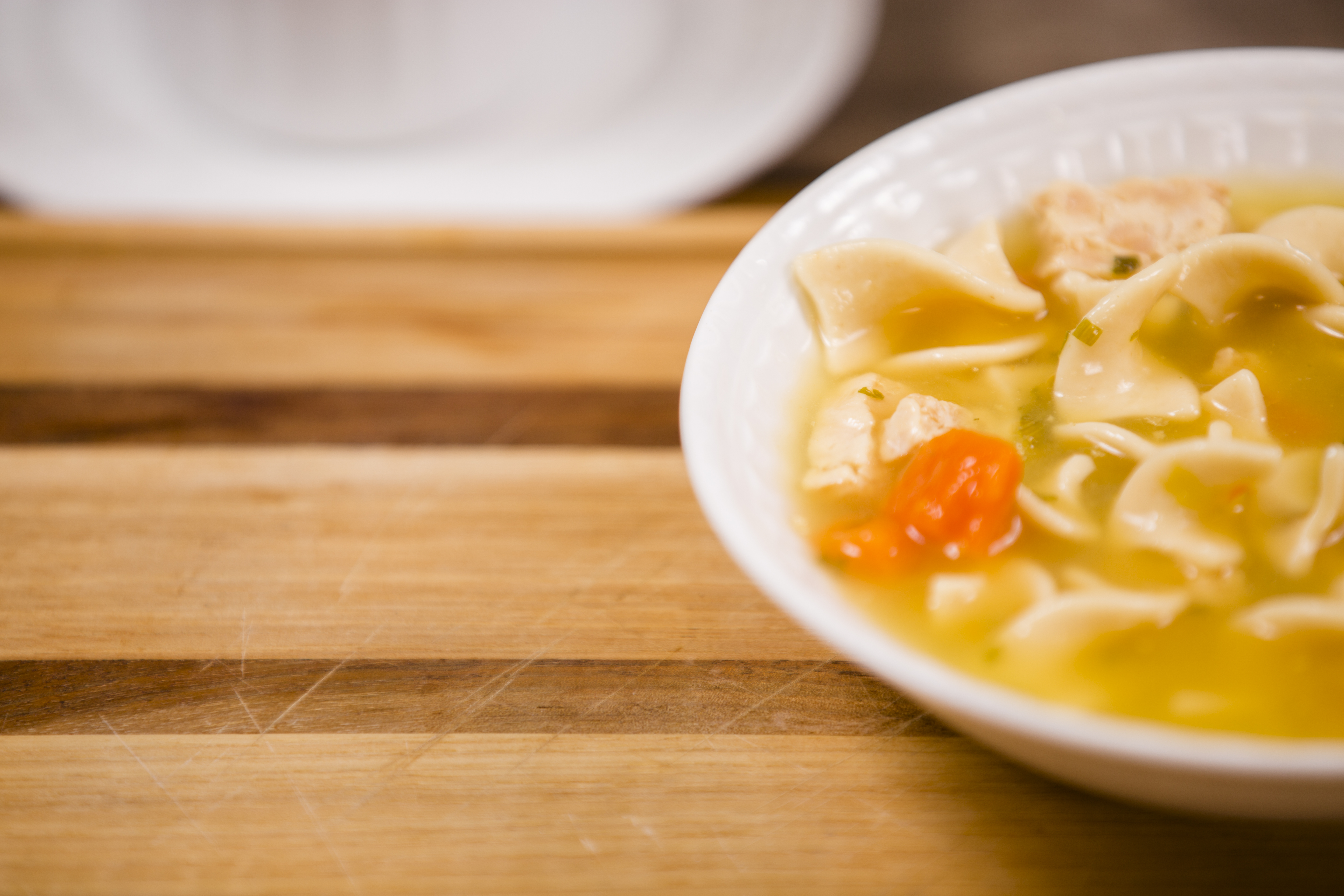 Chicken noodle soup in bowl on wooden cutting board. Copyspace.