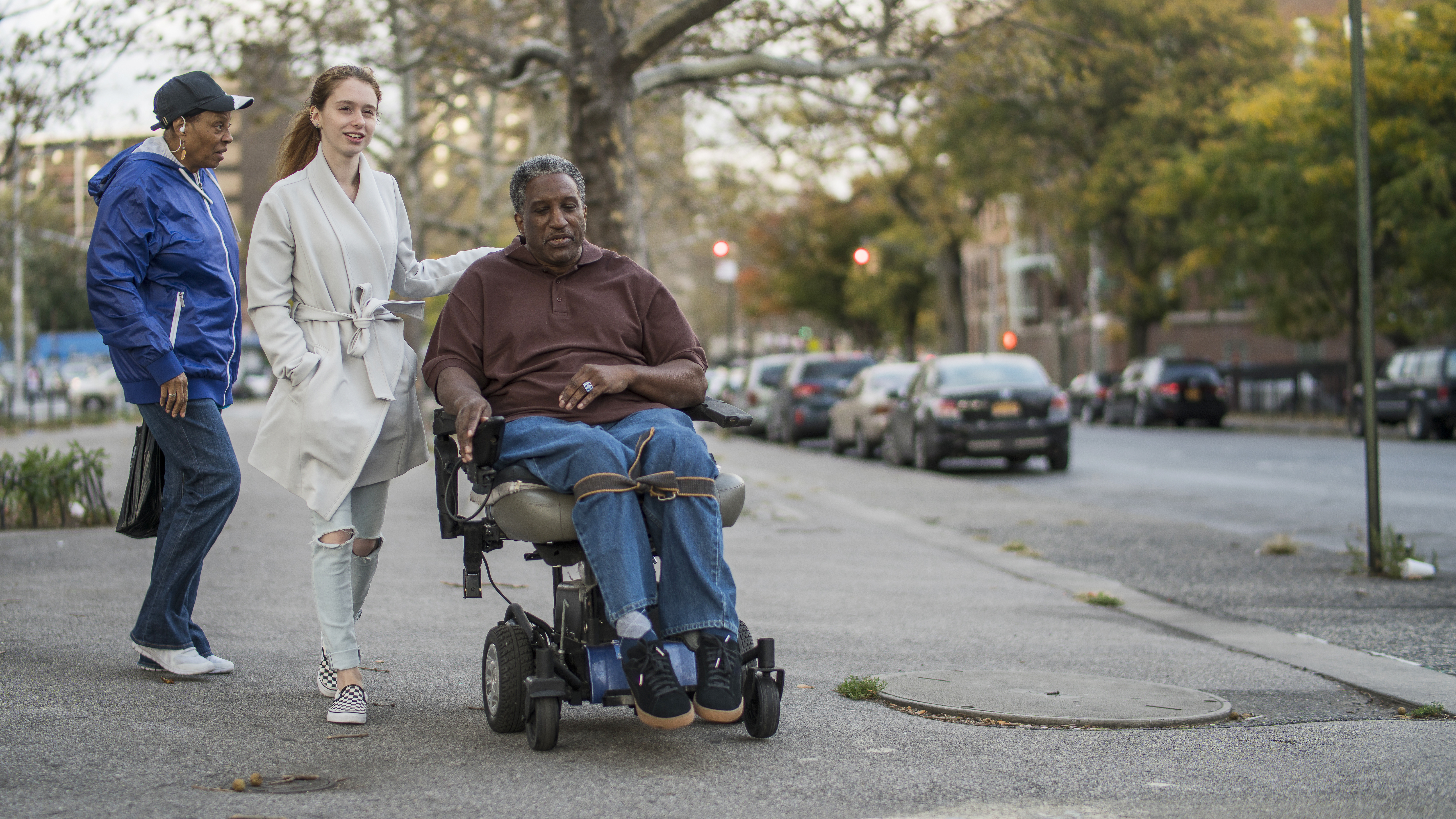 The White teenager girl talking with disabled wheel-chaired African American man and woman when they walking on the street together