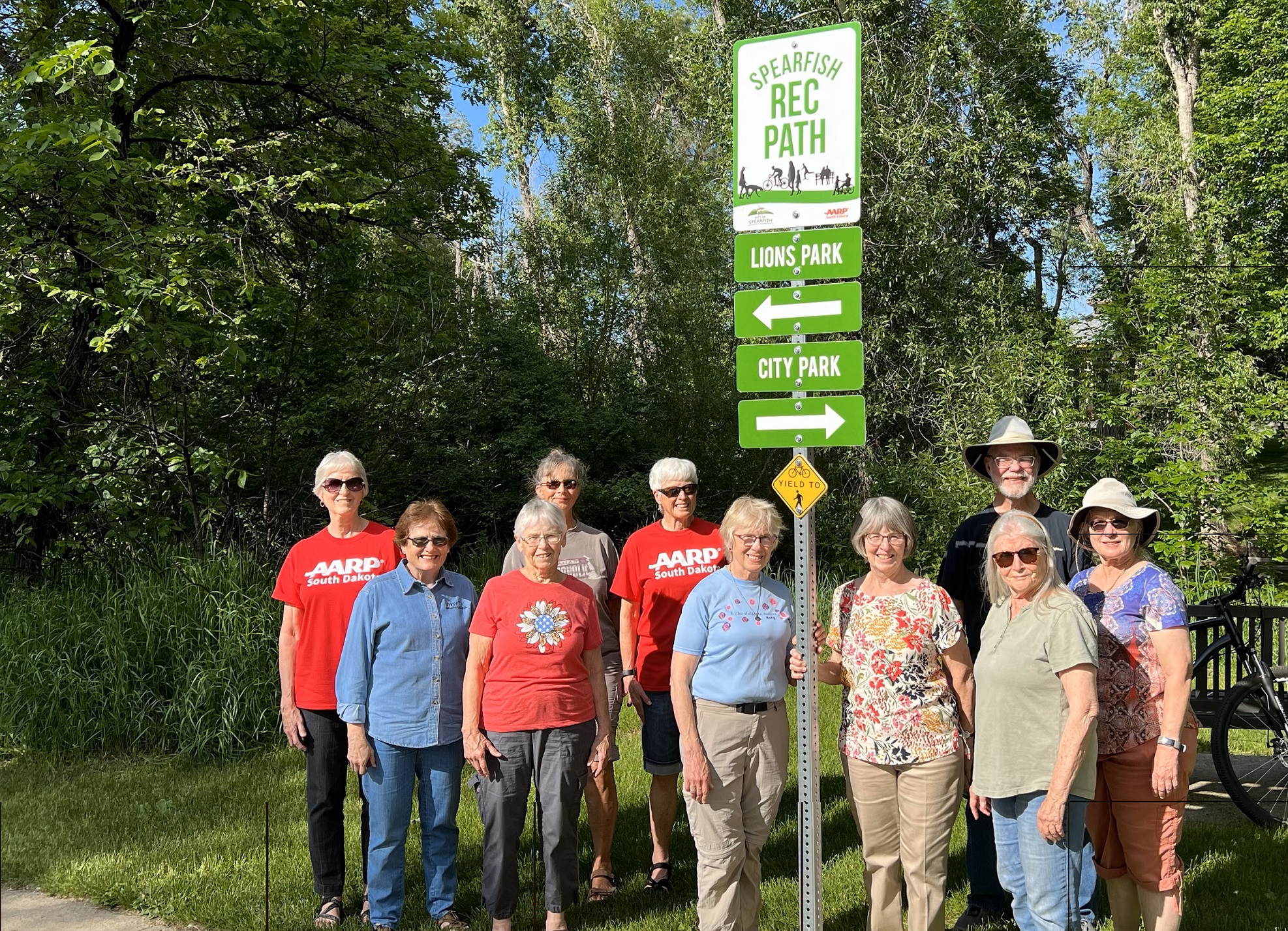 group of 10 volunteers from Spearfish, SD, standing near one of the trail signs they placed in a local park