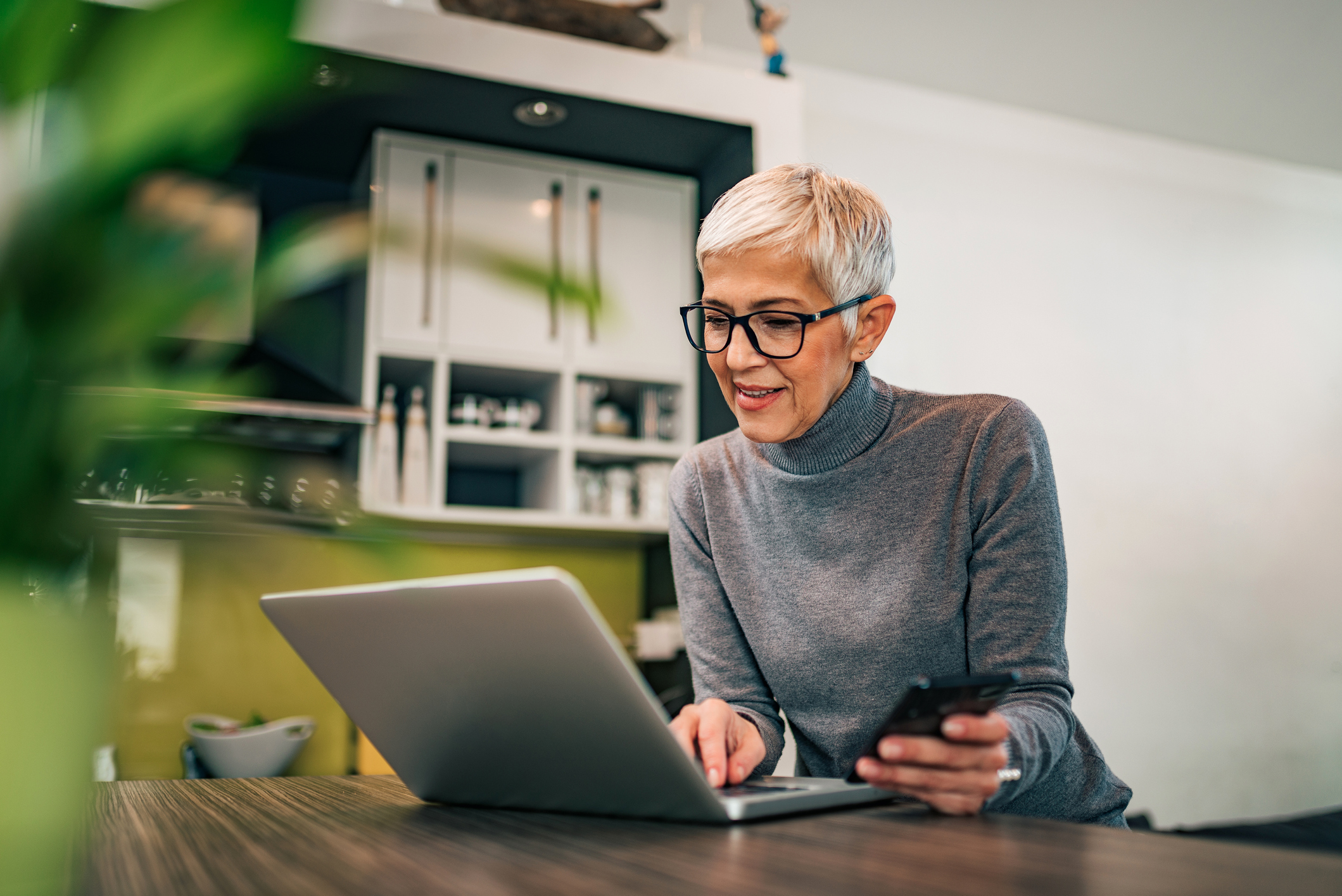 Modern mature woman using laptop and smart phone at home, portrait.