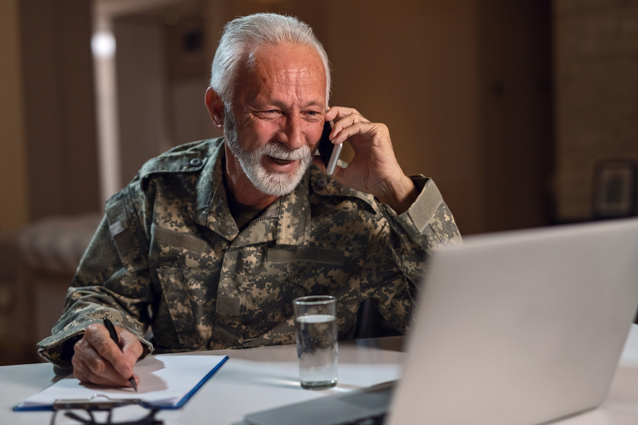 Happy mature army soldier working in the office and talking on the phone.