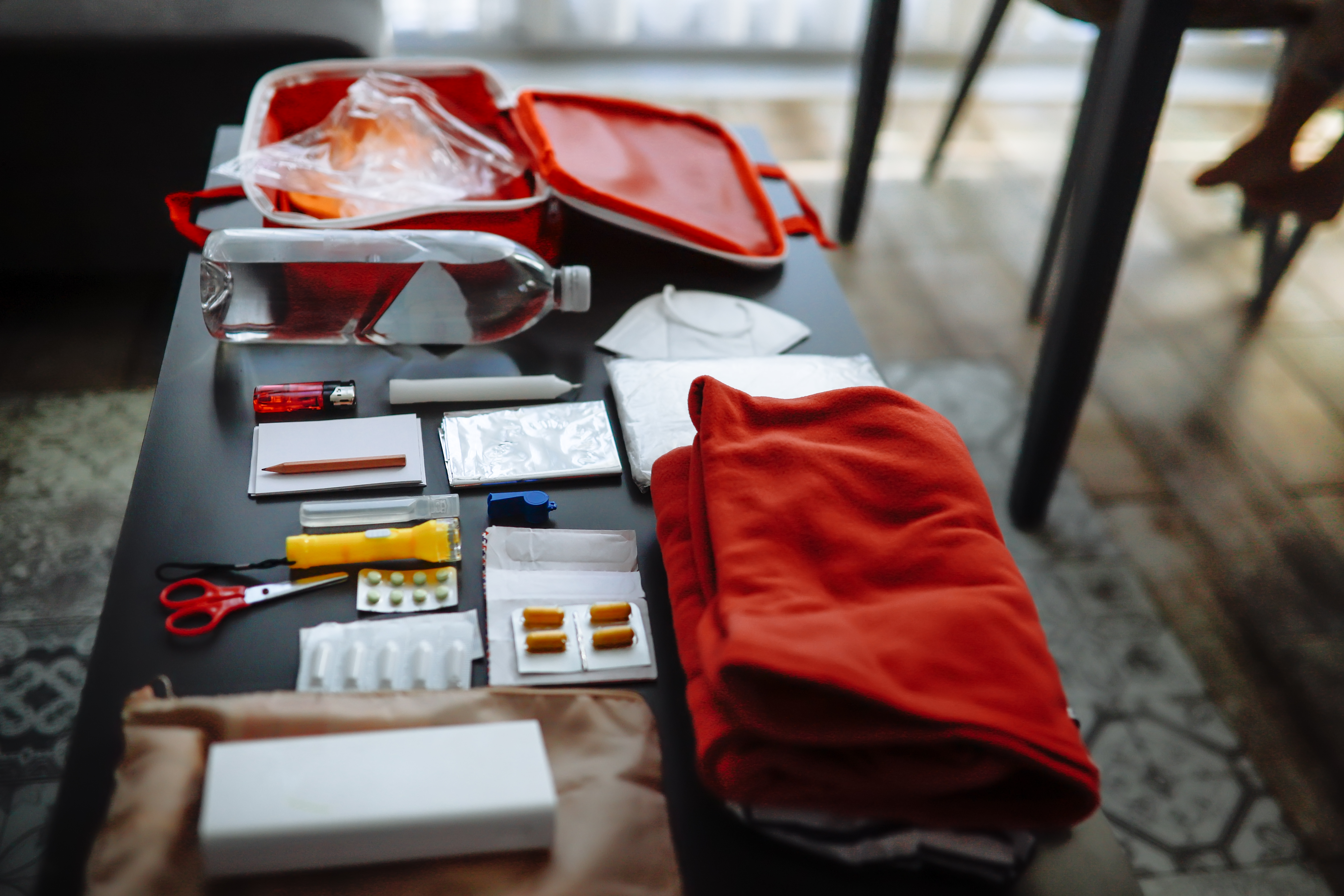 prepping essentials: water, protective gear, whistle, raincoat, and tools for emergencies, shown in a cozy home flat lay.