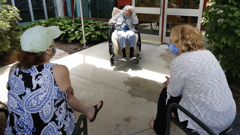 Two woman wearing face masks visiting their mother outside of a